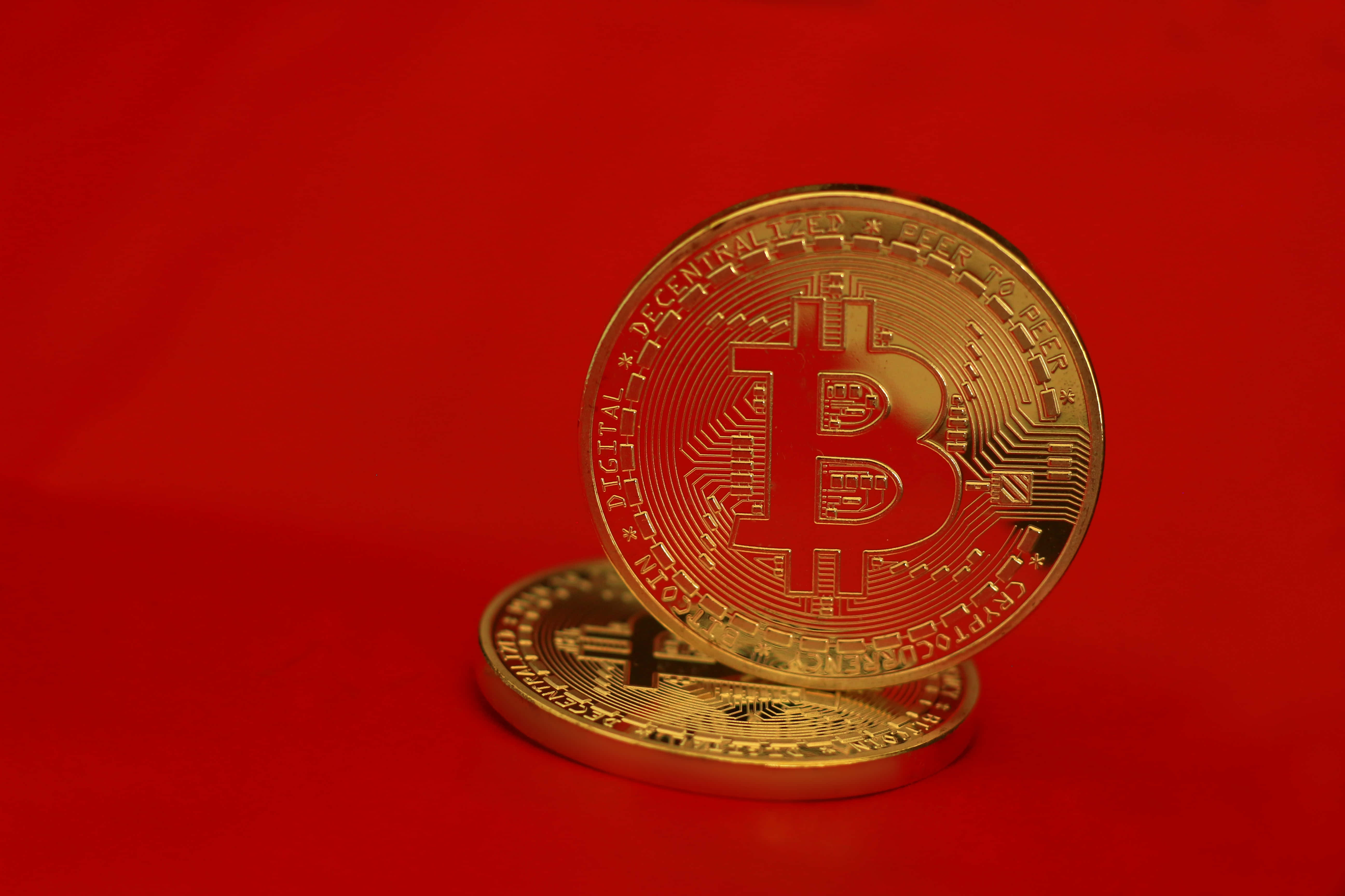 Mining 桌布 壁紙 — 兩枚閃閃發光的金色比特幣硬幣放在鮮紅色的背景上，一枚直立，另一枚平躺。