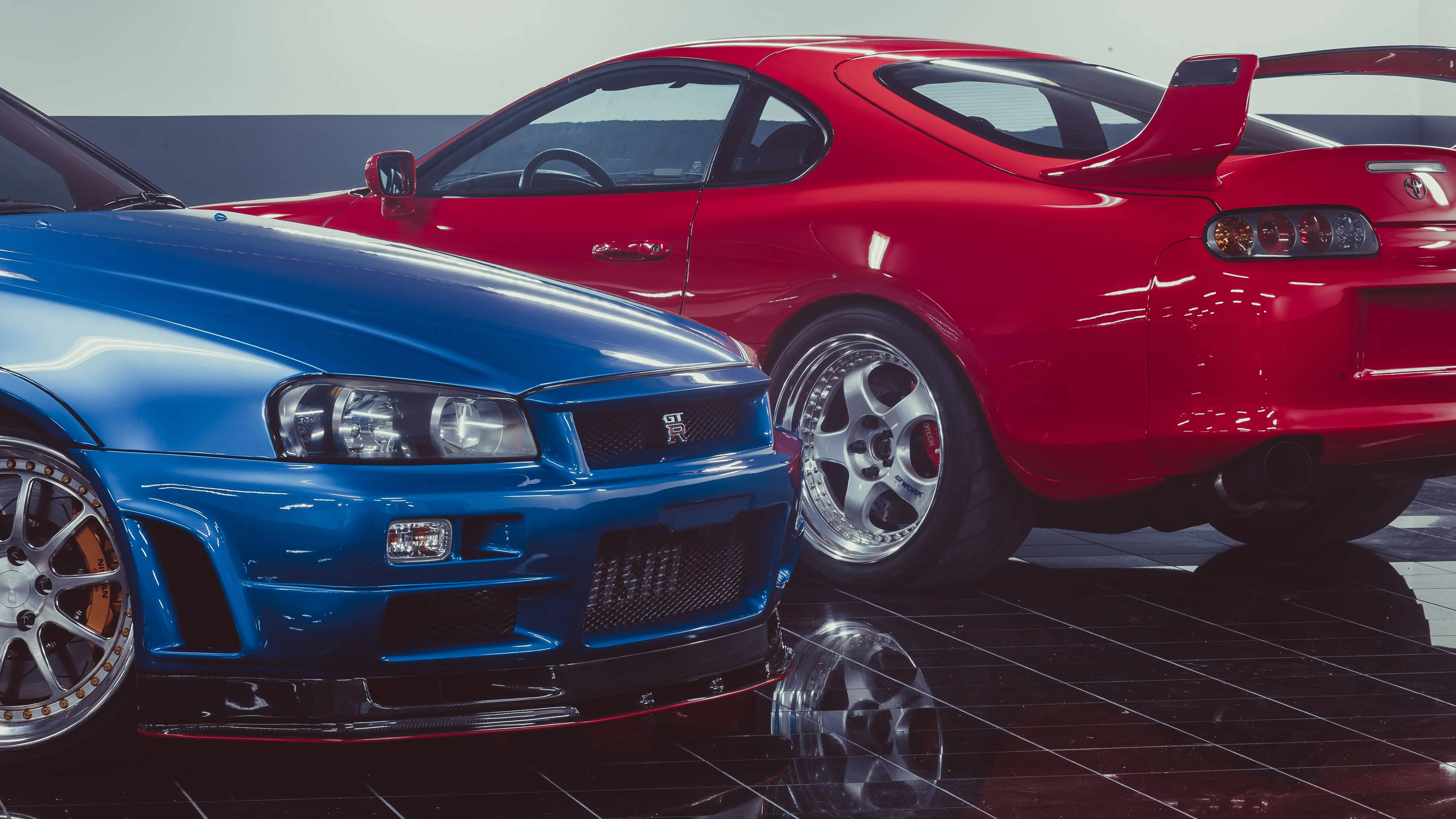 Nissan 桌布 壁紙 — 兩架光面跑車，一架藍色日產GT-R同紅色豐田Supra，泊喺室內反光黑色瓷磚地板上面。