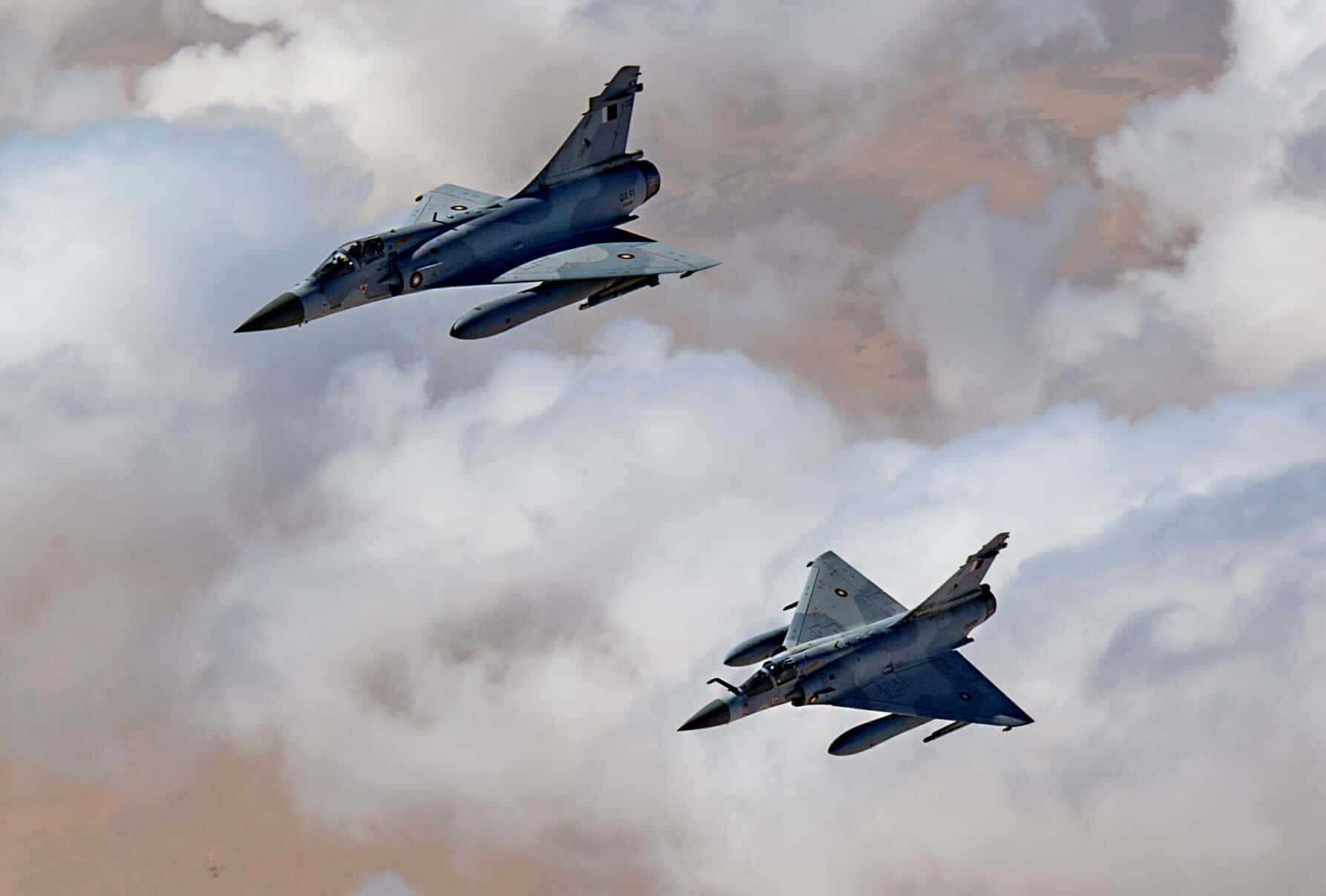 Air Force 桌布 壁紙 — 兩架戰鬥機在多雲的天空中翱翔，下方可見沙漠景觀。