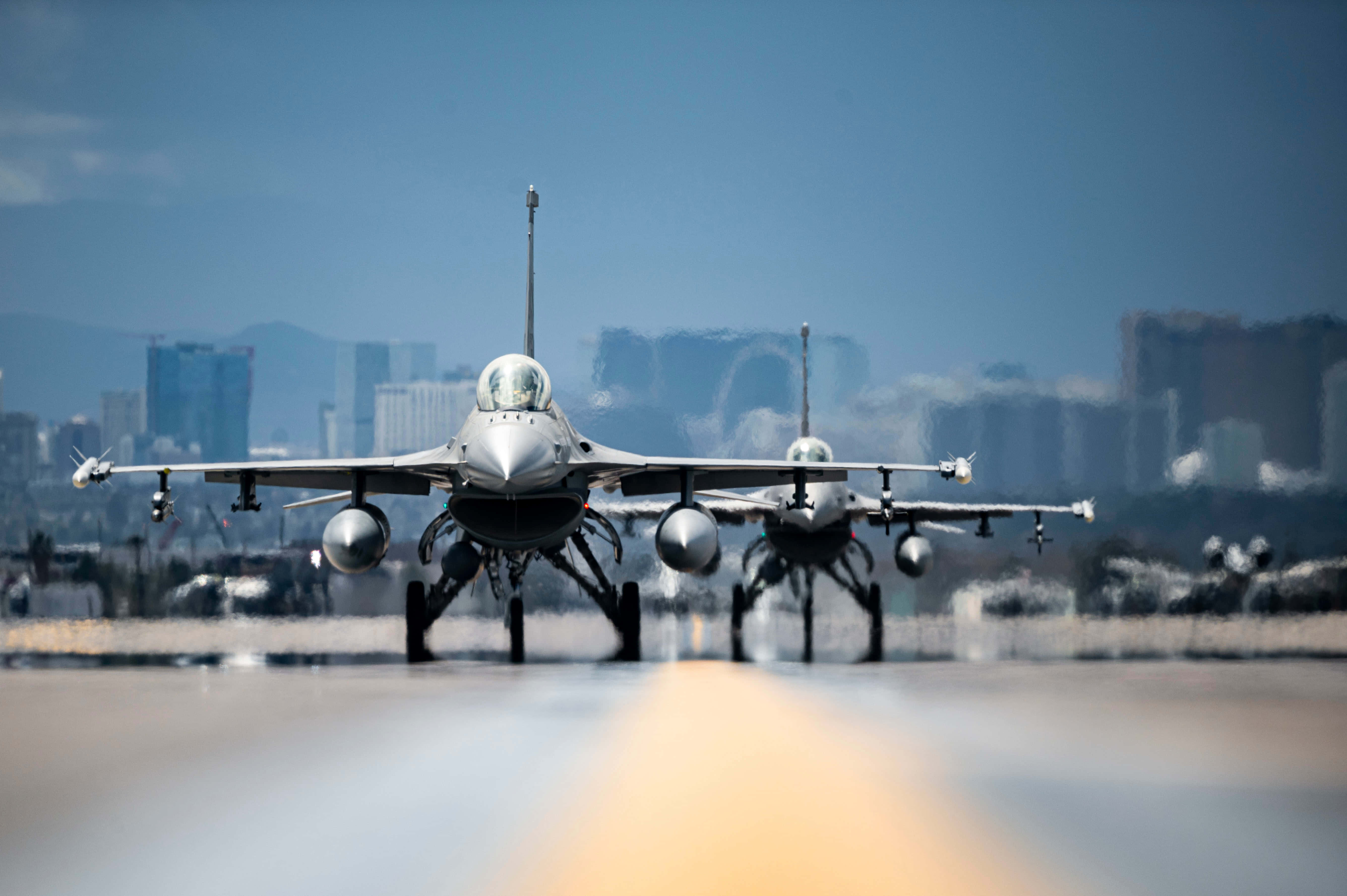 空軍 桌布 壁紙 — 兩架戰鬥機在跑道上，背景是晴朗藍天下的城市天際線。