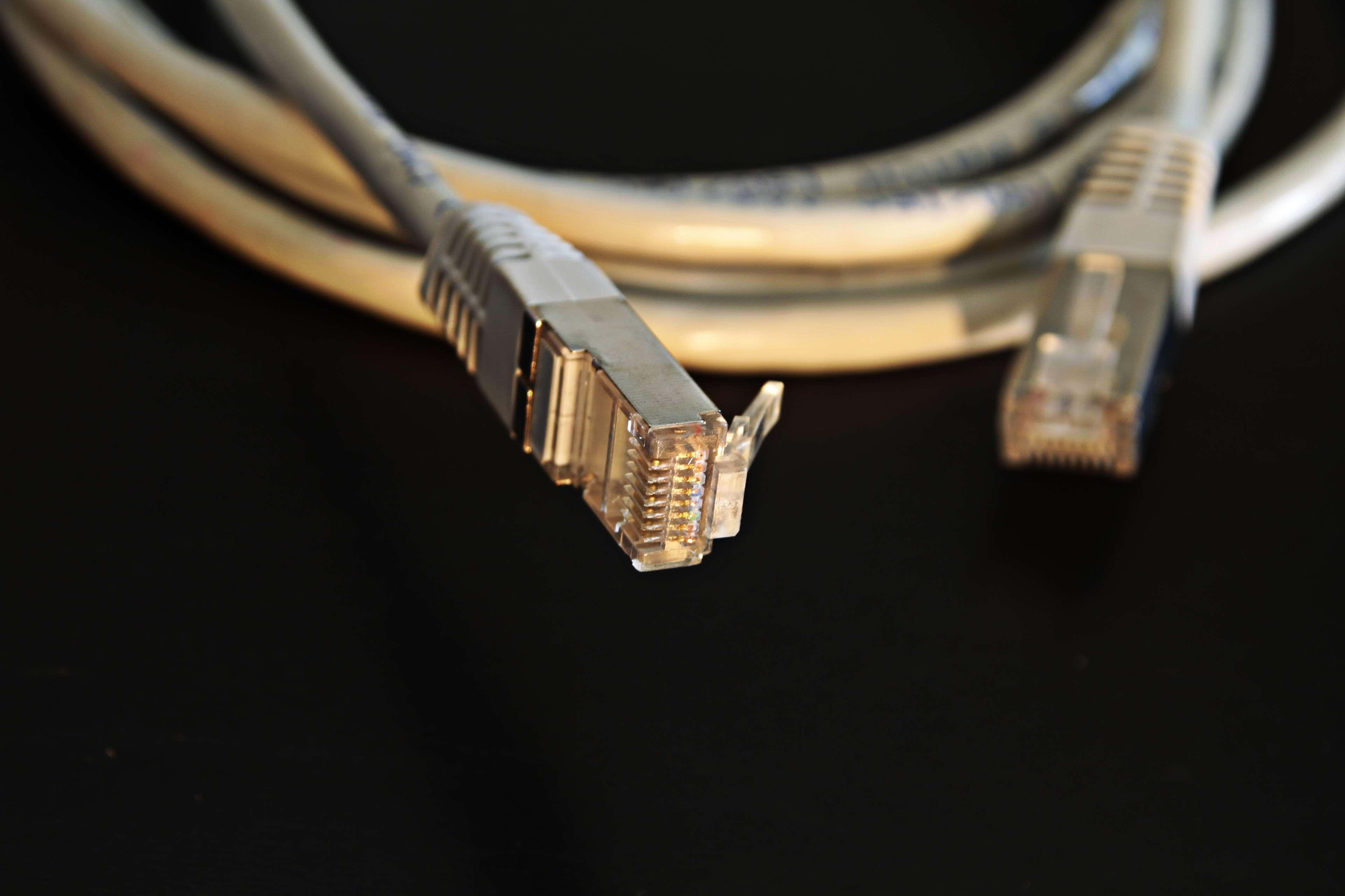 Ethernet 桌布 壁紙 — 兩條以太網電纜盤繞在黑色表面上，對連接器進行銳利對焦的特寫。