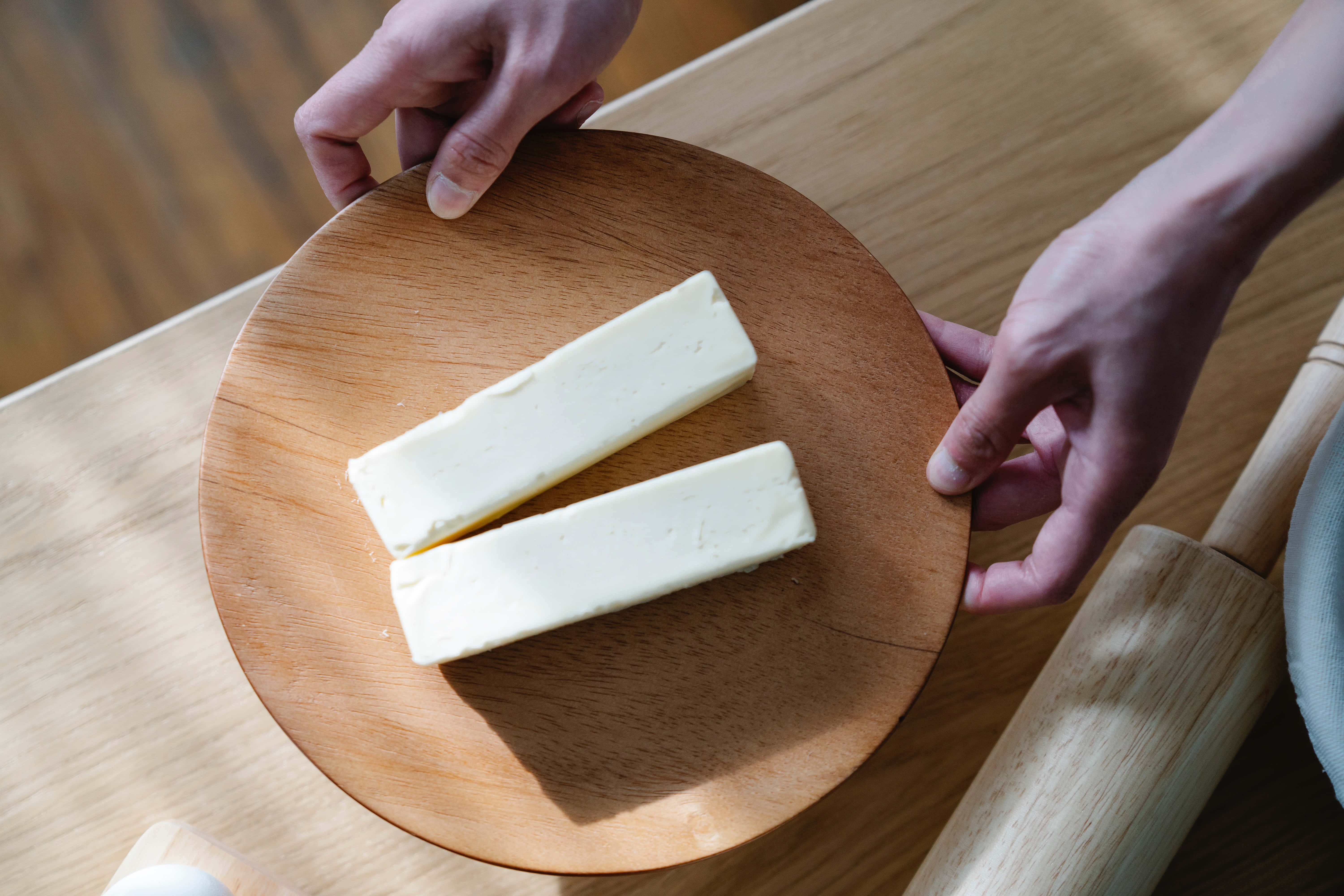 Cheese 桌布 壁紙 — 兩條牛油放在一個由手拿著嘅木板上，喺一個溫暖嘅廚房環境中。