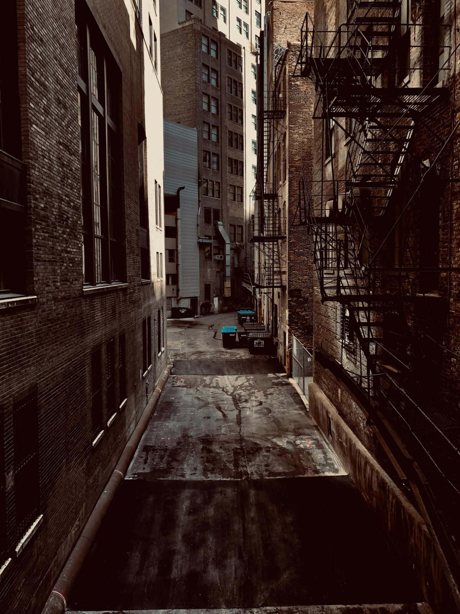 Alleyway 桌布 壁紙 — 兩棟磚建築之間狹窄的城市小巷，設有逃生梯和垃圾箱，沐浴在溫暖的金色光線下。