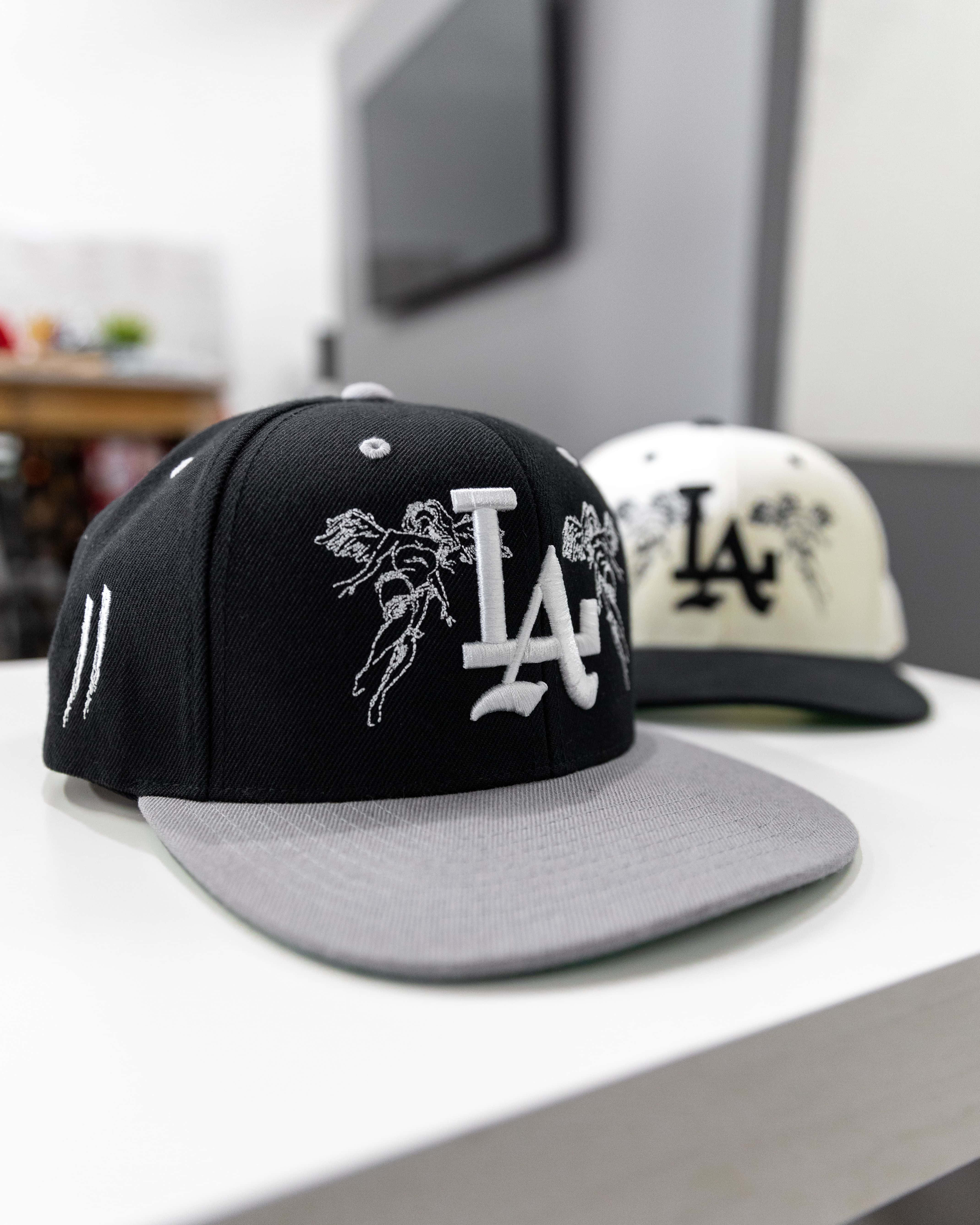 Hat 桌布 壁紙 — 兩款時尚的 snapback 帽，帶有 LA 標誌和天使刺繡，放置在現代房間的白色架子上。