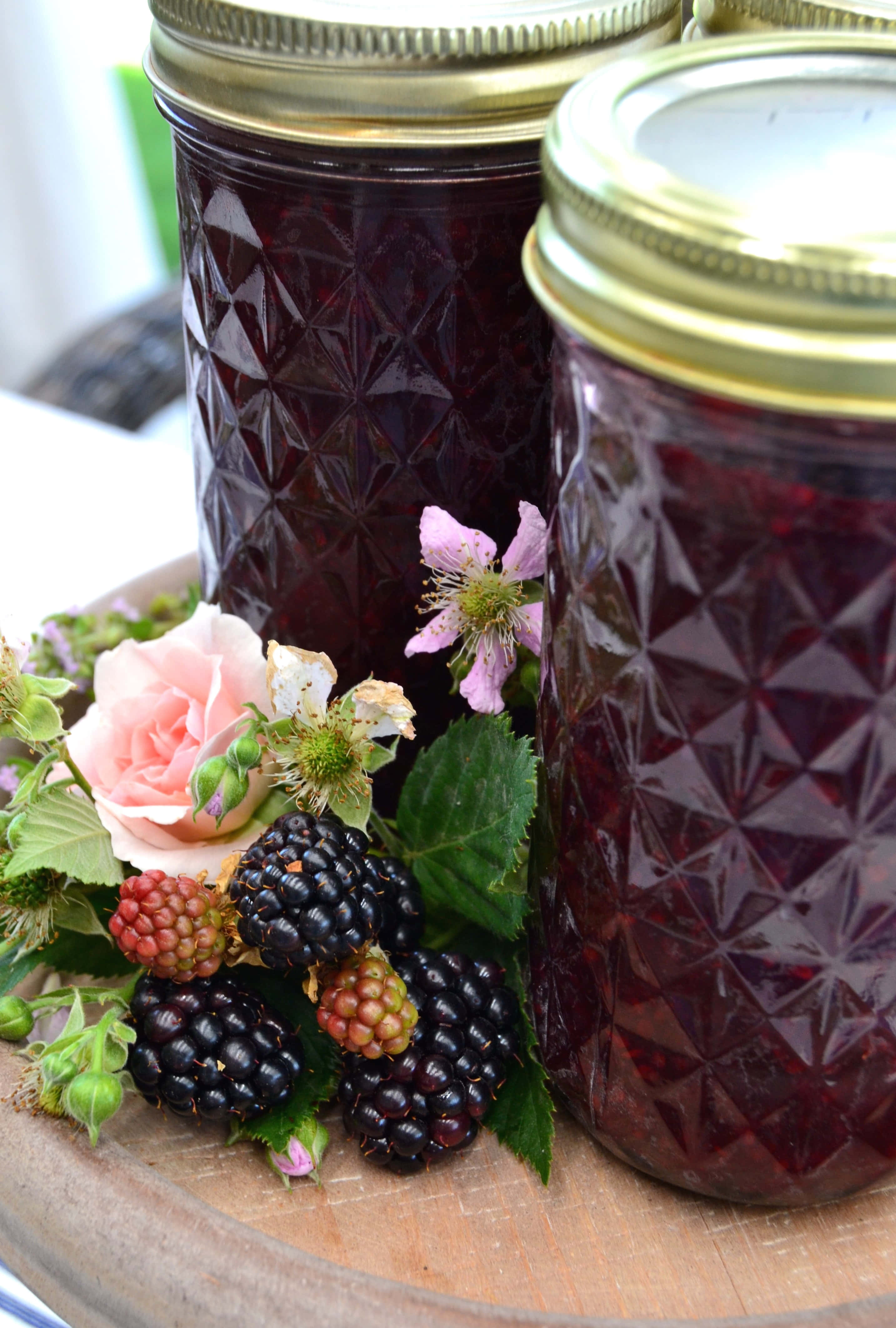 Blackberry Jam 桌布 壁紙 — 兩玻璃樽深色莓果醬放在木托盤上，旁邊是新鮮黑莓和精緻的粉紅色花朵。