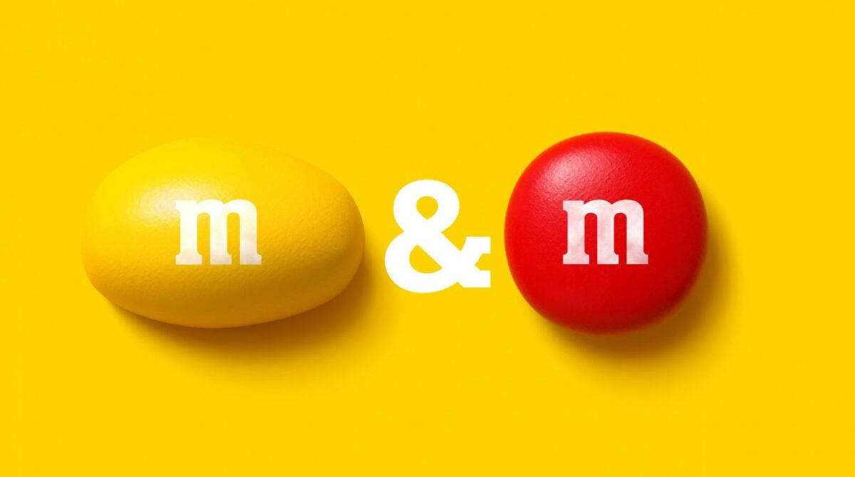 Chocolate 桌布 壁紙 — 兩粒光澤嘅M&M糖果黃色同紅色，帶有白色m標誌，並排喺充滿活力嘅黃色背景上。