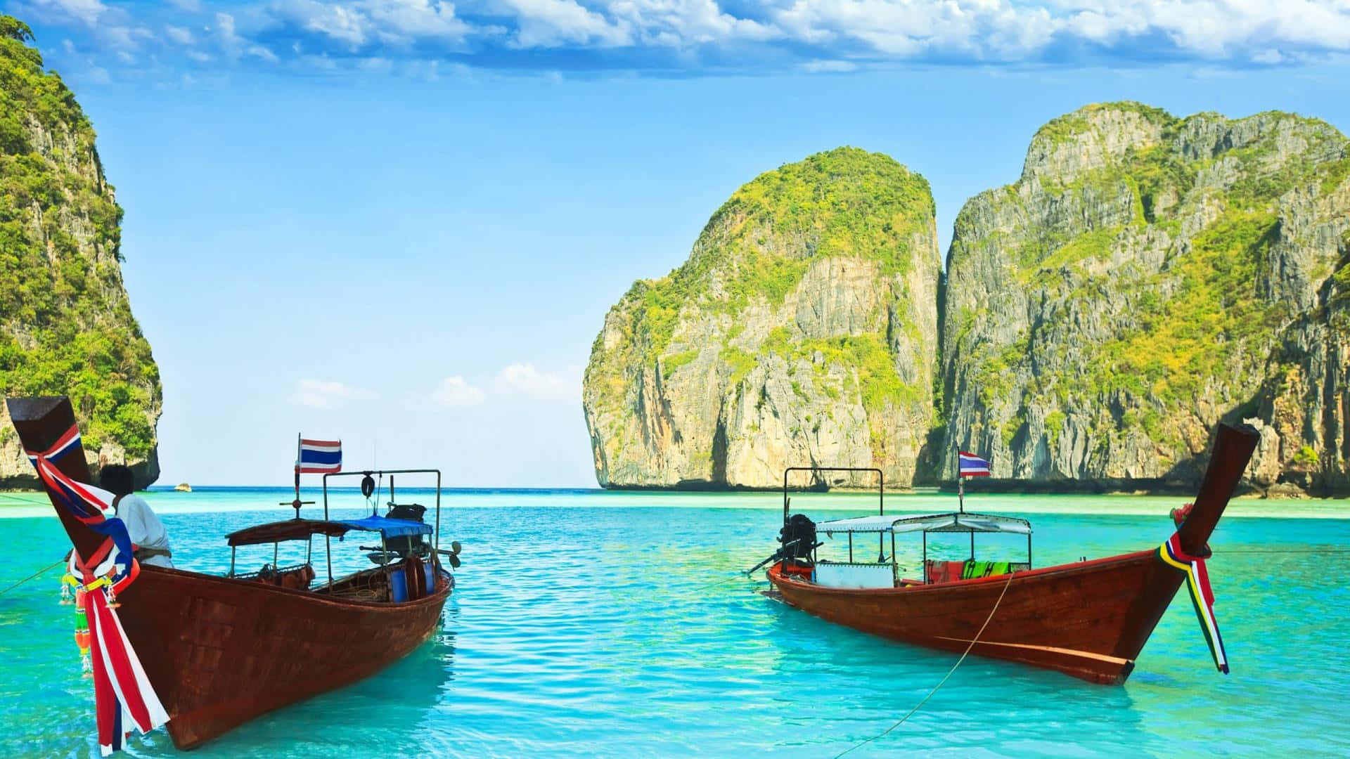 Thailand Beach 桌布 壁紙 — 兩艘傳統泰國長尾船在清澈碧綠的海水中靜靜漂浮，四周是高聳的綠色懸崖，上方是明亮的藍天。