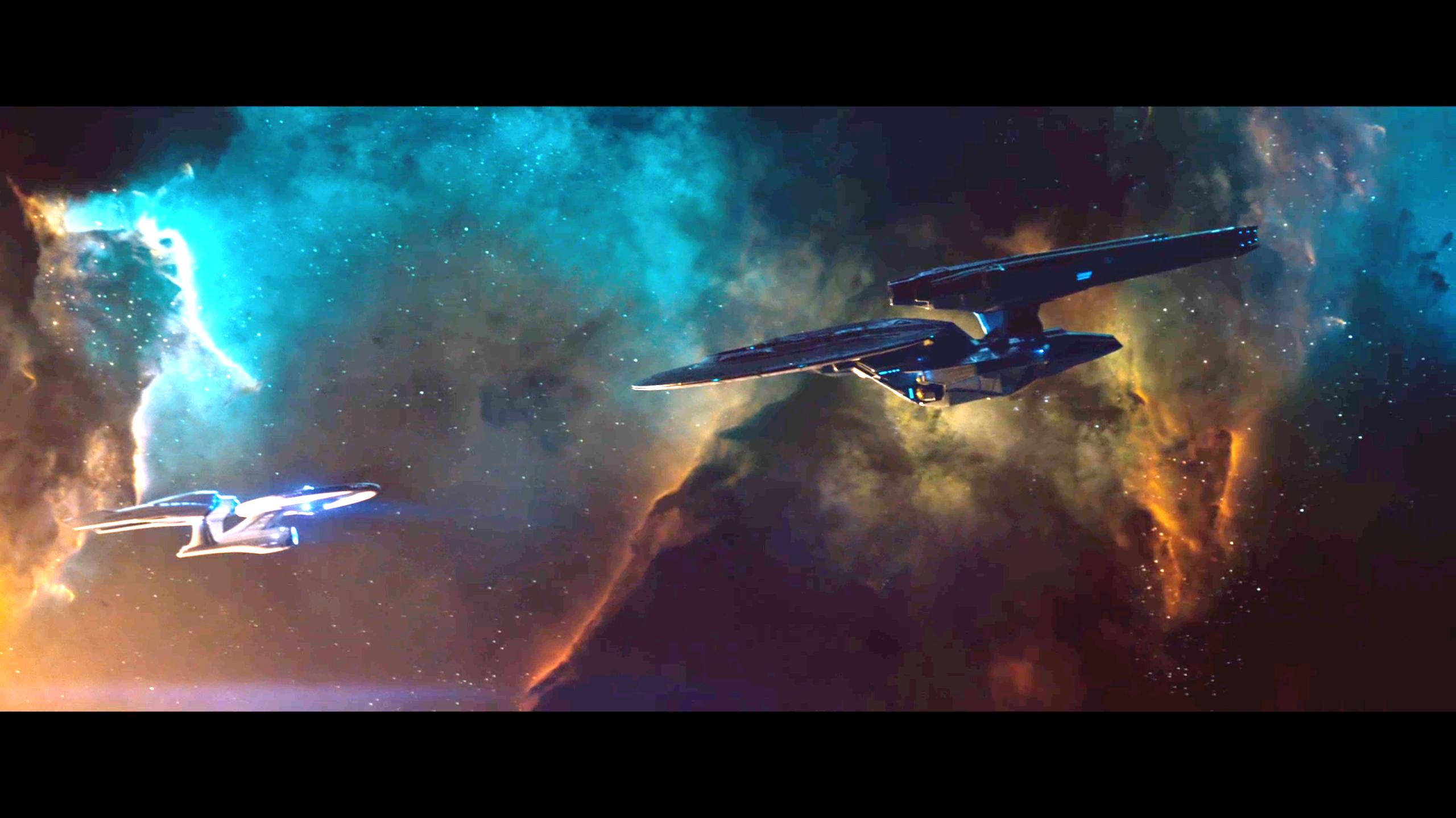 兩艘經典星艦正面對決 壁紙 — 兩艘星際飛船在充滿活力的星雲中翱翔，星雲中有旋轉的藍綠色和橙色宇宙雲以及發光的星星。