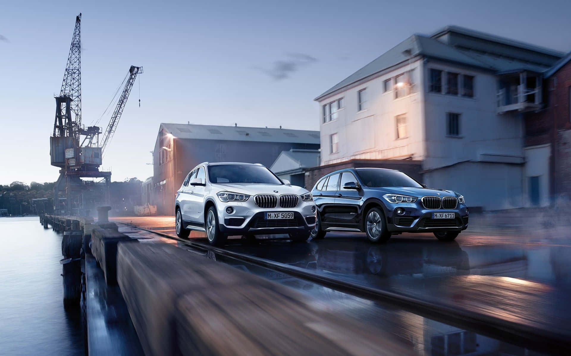Bmw I8 桌布 壁紙 — 兩輛BMW SUV在黃昏時分的濕潤碼頭上閃耀，背景有起重機和工業建築。