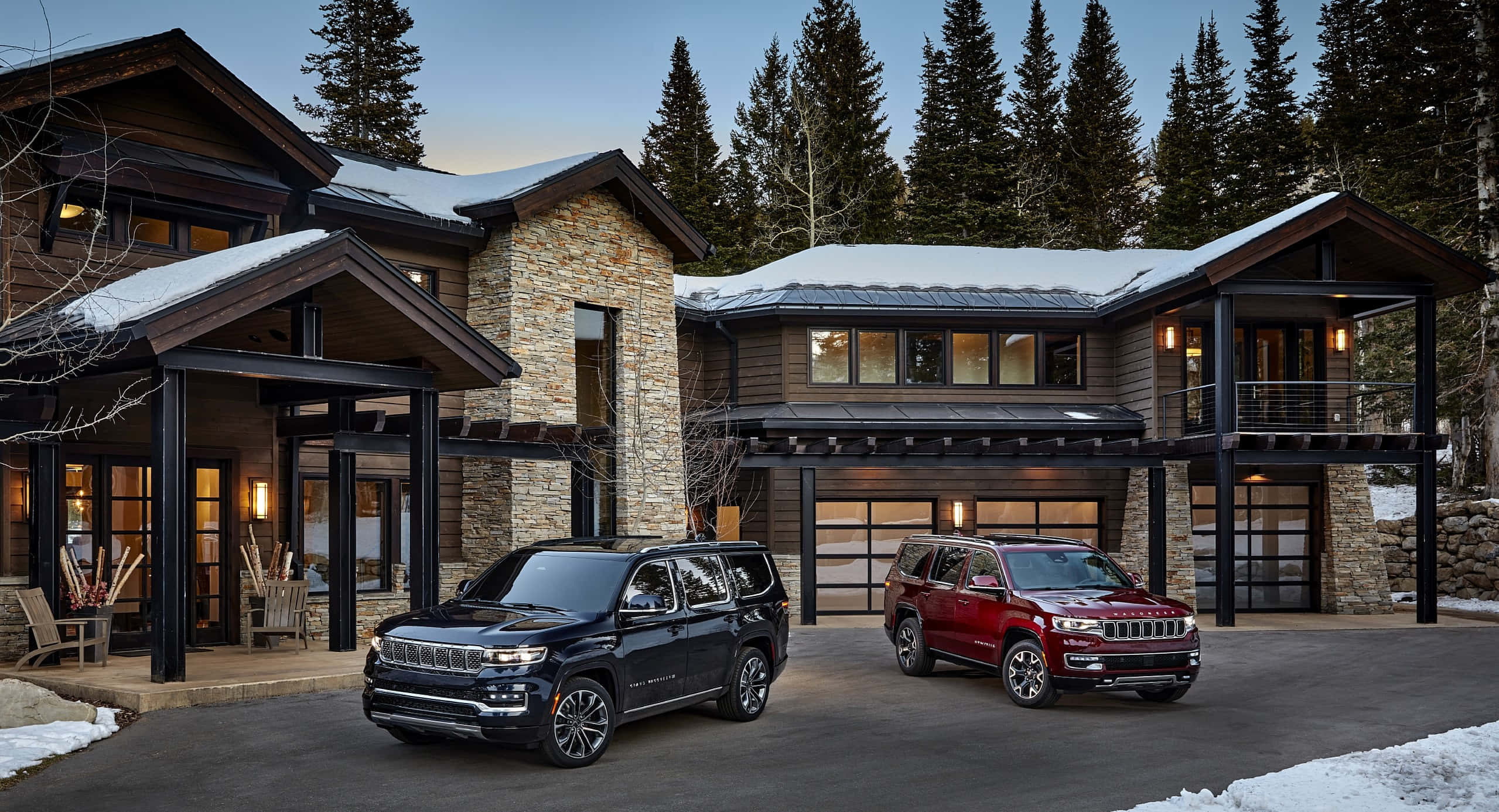 Jeep Wagoneer 桌布 壁紙 — 兩輛Jeep SUV停在一間覆蓋著薄雪、帶有發光窗戶和常綠樹的現代山間小屋前。