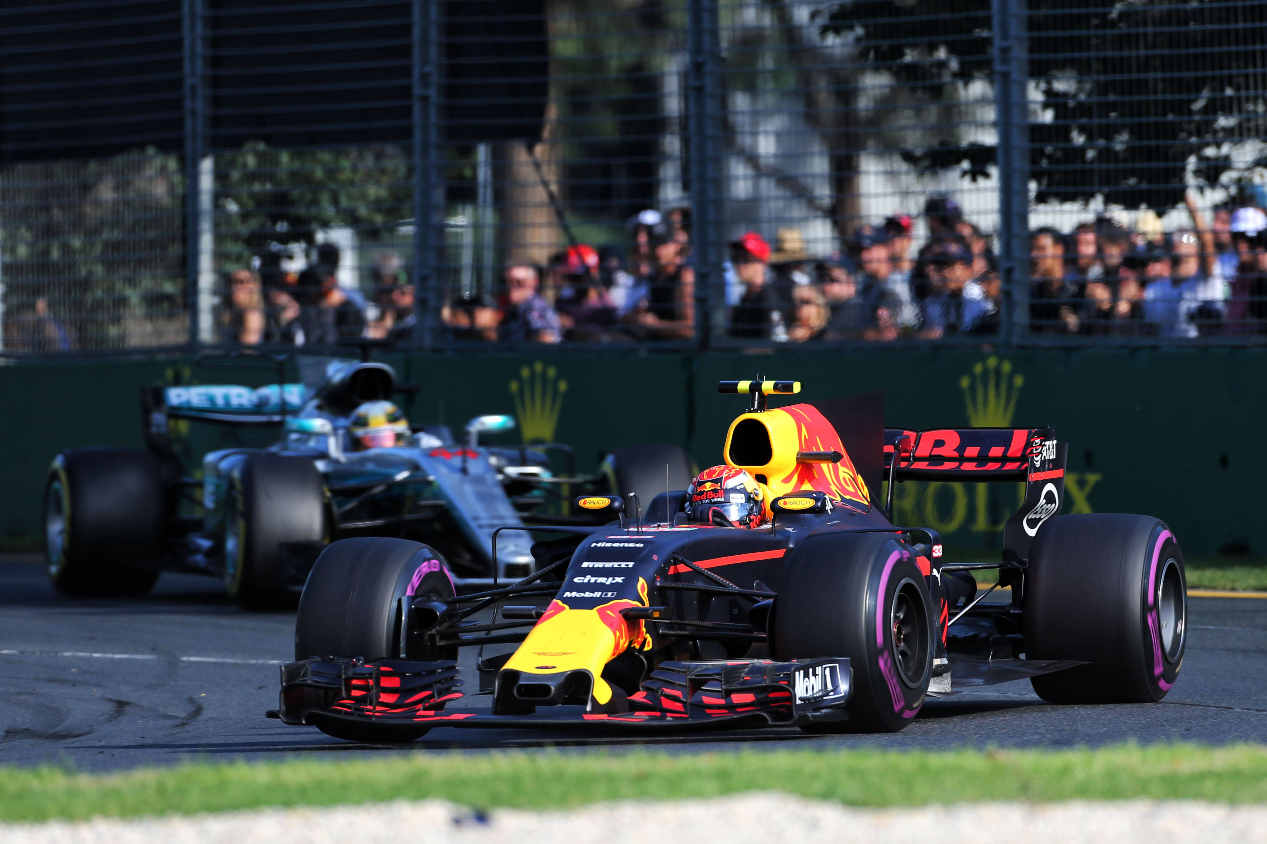 Verstappen 桌布 壁紙 — 兩輛一級方程式賽車在陽光照耀的賽道上並排競速，觀眾在圍欄後面觀看。