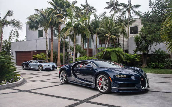 兩輛Bugatti超級跑車停泊在瓷磚車道上，背景有棕櫚樹和現代房屋。