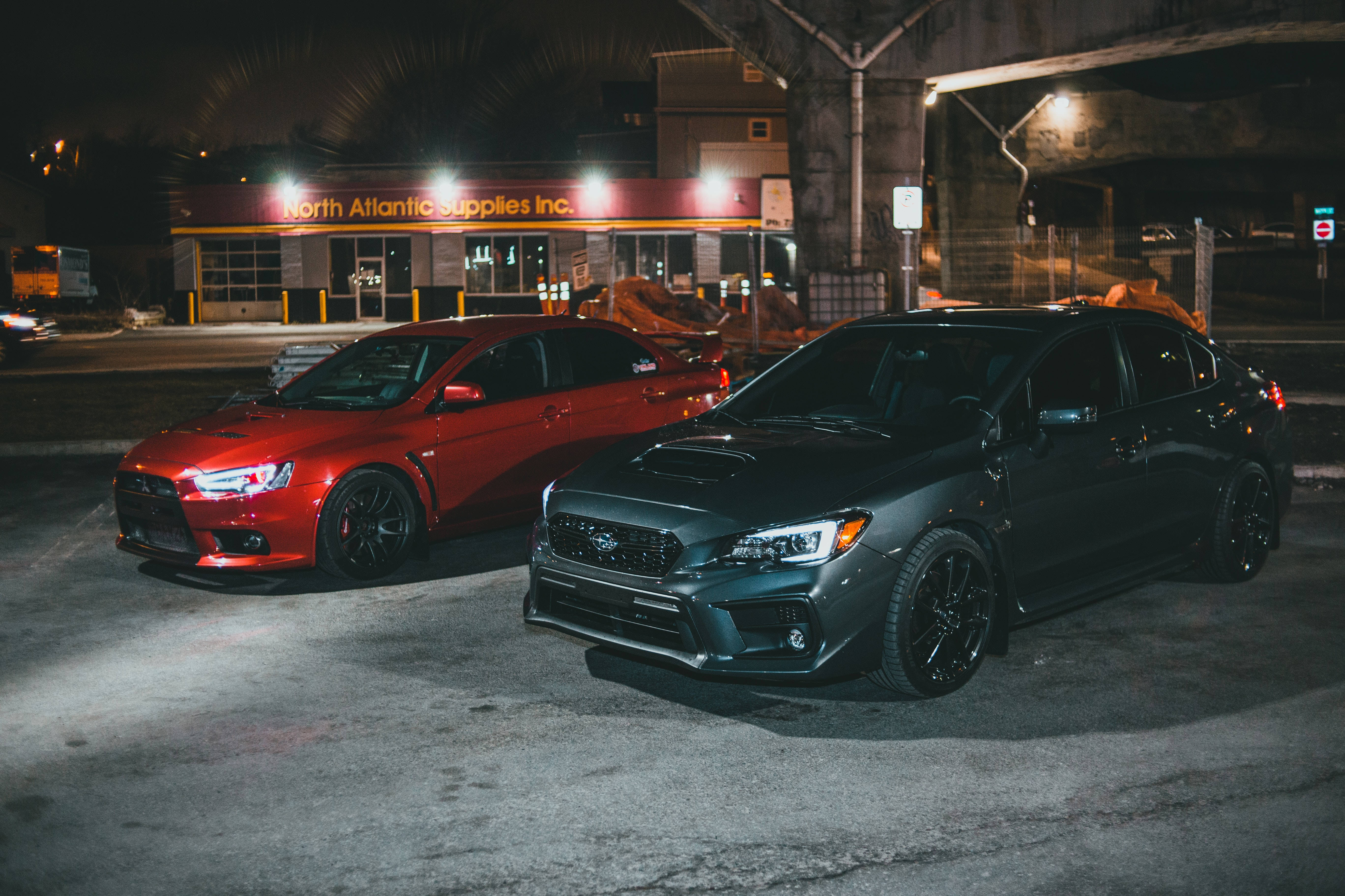 4K 桌布 壁紙 — 兩輛改裝的Subaru房車在夜間停泊在橋下，發光的車頭燈和城市街燈在潮濕的路面上投射出倒影。