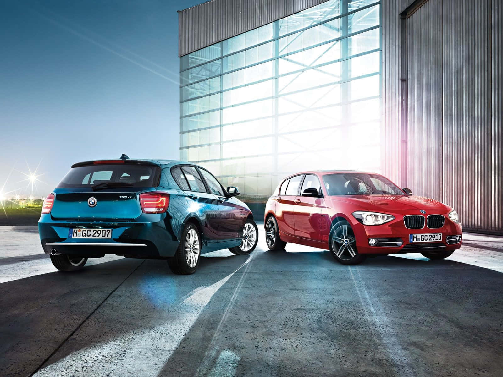 Bmw 1 Series 桌布 壁紙 — 兩輛時尚的BMW，一藍一紅，停在一座現代玻璃和金屬建築前，在明亮的日光下。