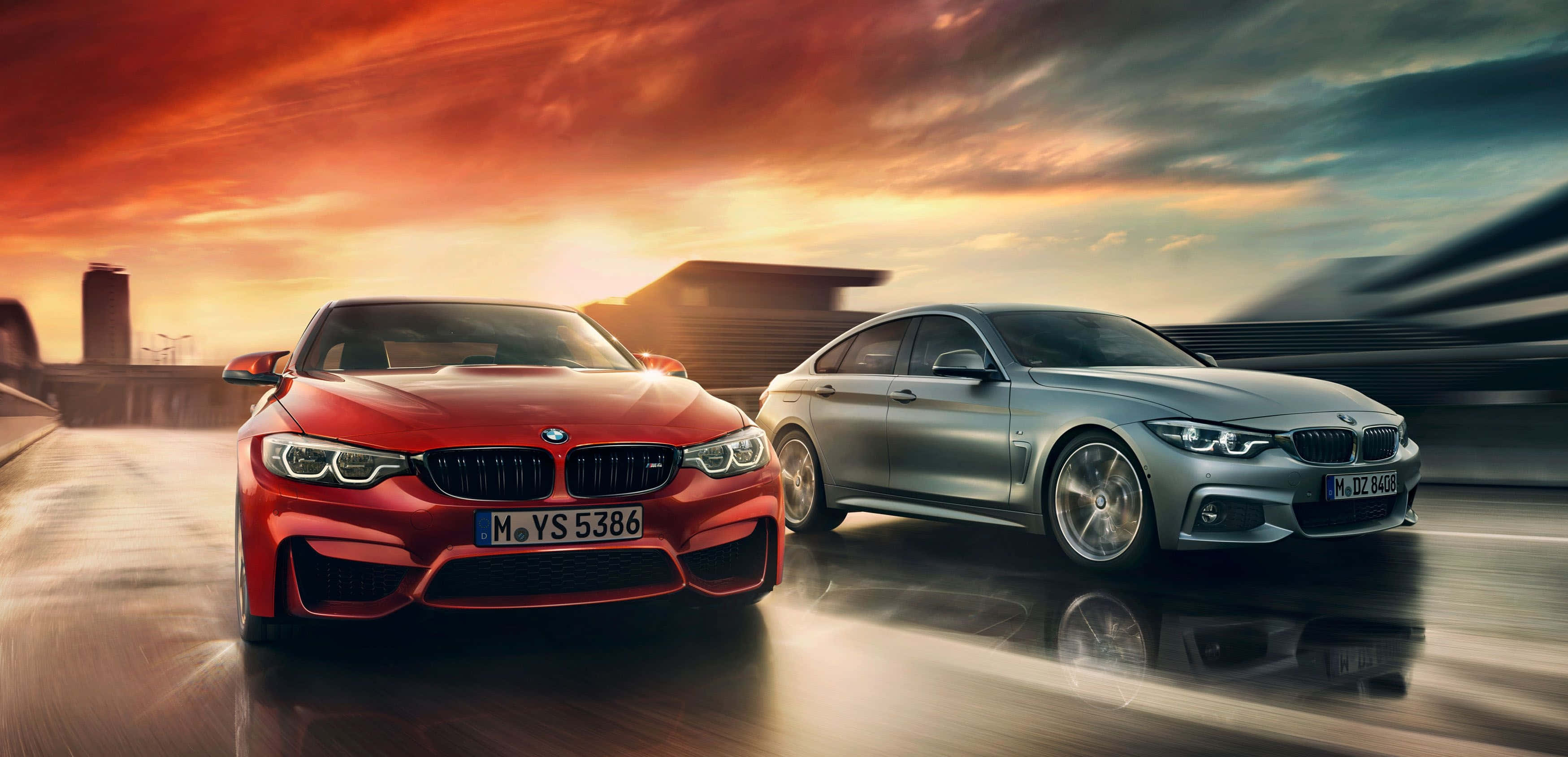 Bmw 4 Series 桌布 壁紙 — 兩輛時尚的BMW雙門轎跑車，一紅一銀，在潮濕的道路上並肩奔馳，背景是火紅的夕陽天空。