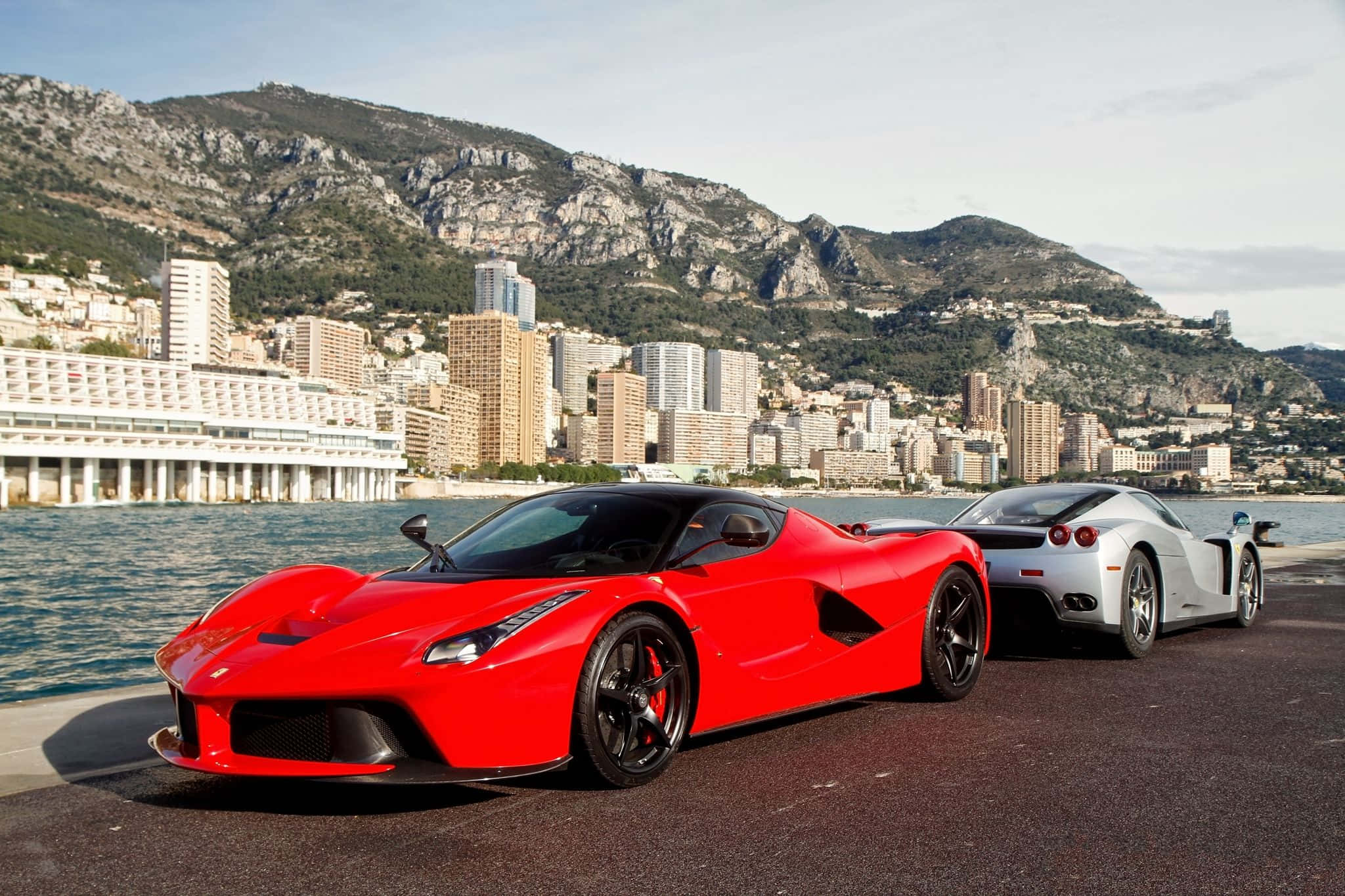 Ferrari Laferrari 桌布 壁紙 — 兩輛時尚超級跑車，一輛鮮紅色法拉利LaFerrari和一輛銀色法拉利Enzo，停泊在俯瞰摩納哥城市景觀和山脈的海岸公路上。