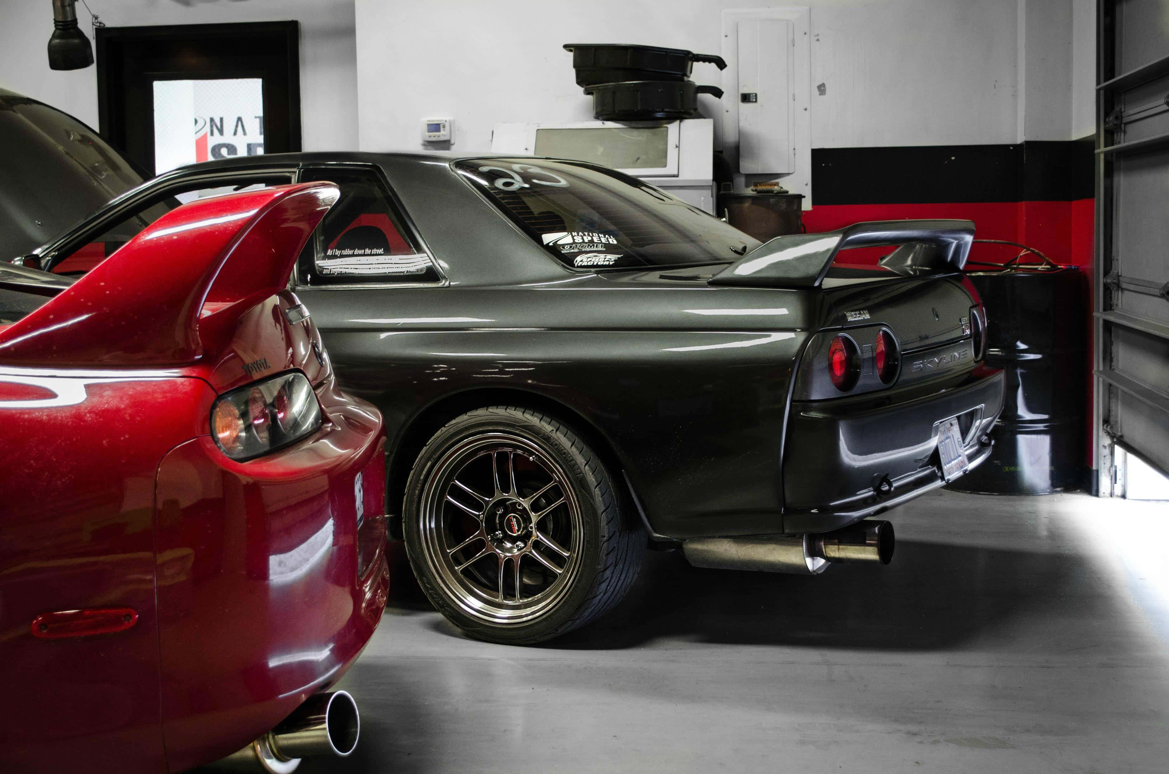 JDM 車 桌布 壁紙 — 兩輛時尚跑車，一輛亮紅色和一輛啞光黑色，並排停放在一個乾淨、帶有工業照明的車庫中。