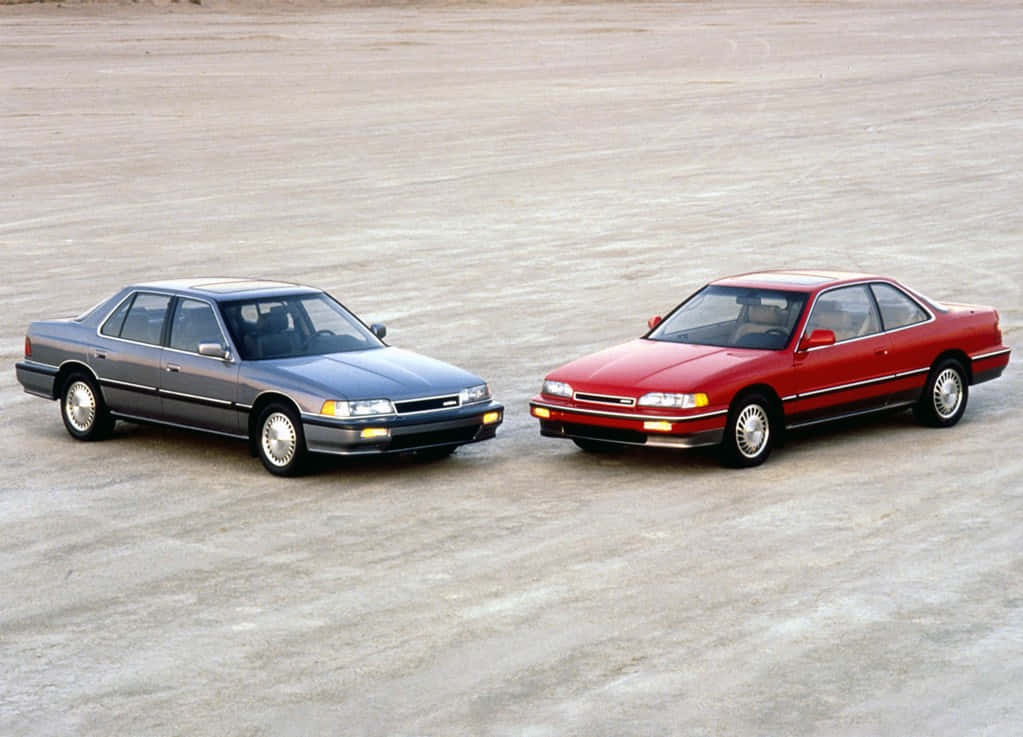 Acura Legend 桌布 壁紙 — 兩輛經典1990年代轎車，一輛藍色四門和一輛紅色雙門跑車，在廣闊空曠的沙漠路面上向前行駛。