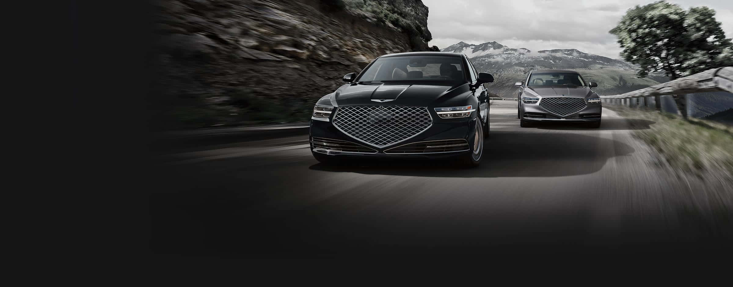 Genesis G90 桌布 壁紙 — 兩輛豪華房車沿著蜿蜒的山路高速行駛，背景是模糊的動態和霧氣繚繞的山峰。