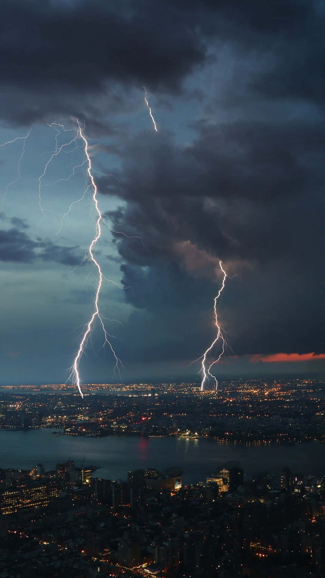 Thunderstorm 桌布 壁紙 — 兩道巨大的閃電劃破暴風雨的天空，照亮了下方燈火輝煌的廣闊城市景觀。