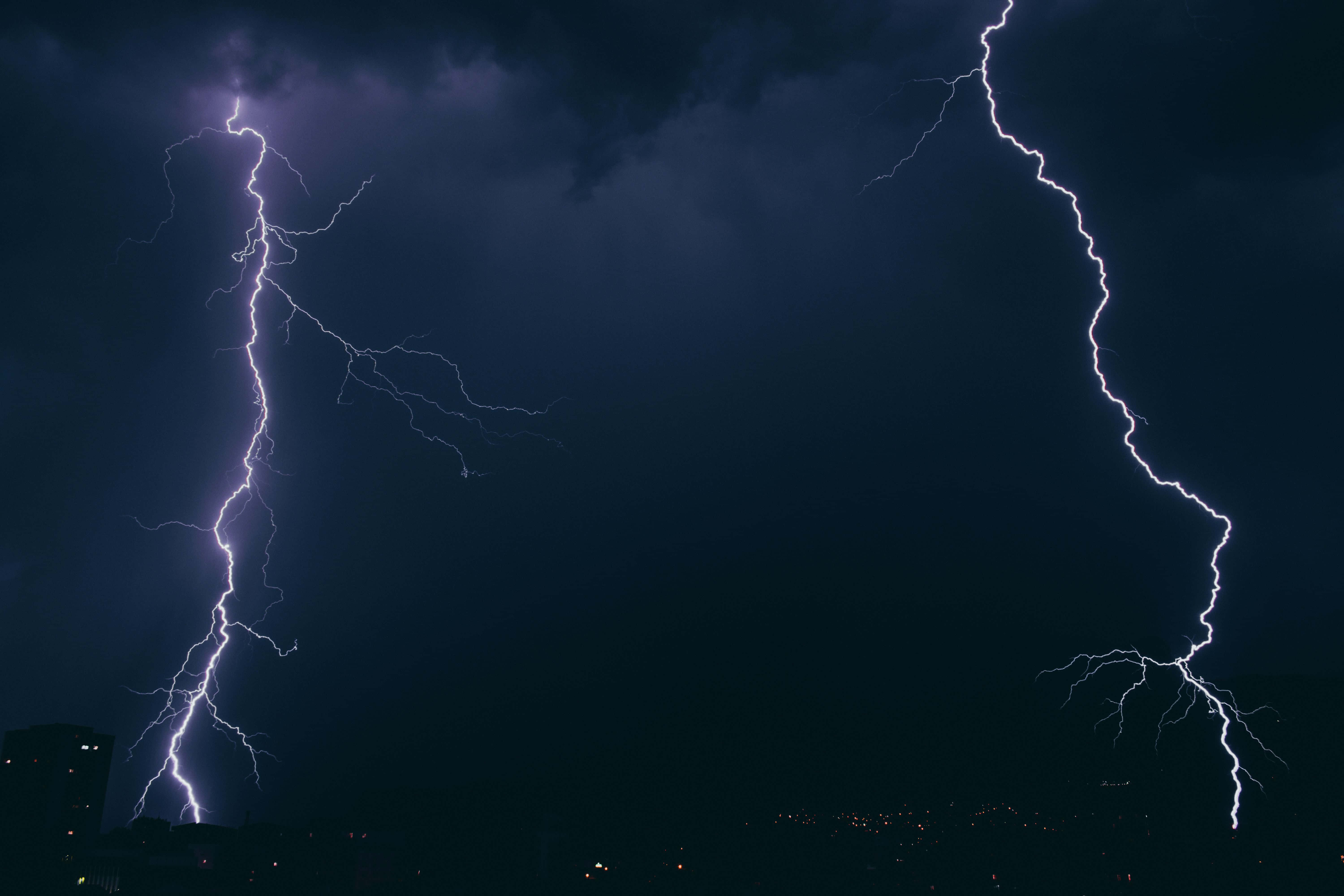 暴風 桌布 壁紙 — 兩道巨大的閃電在夜間城市景觀上方的黑暗暴風雨天空中劈啪作響。