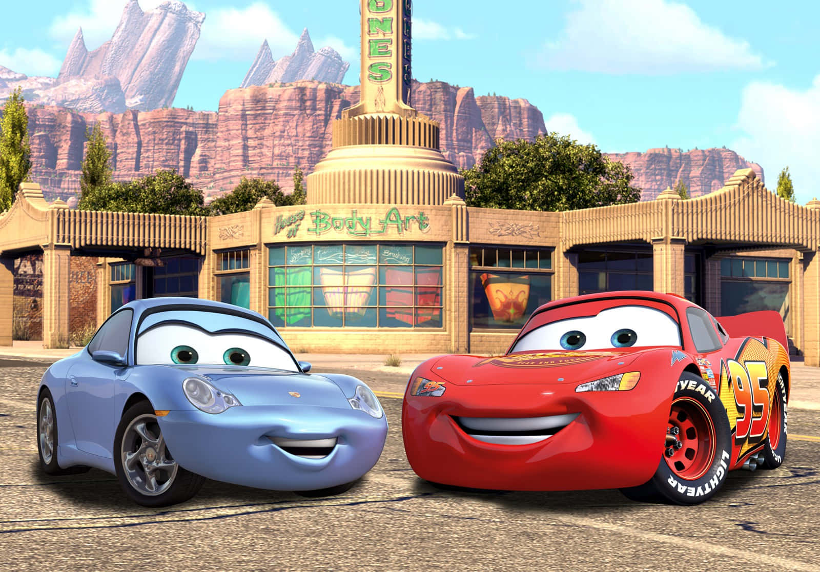 Disney Cars 桌布 壁紙 — 兩部動畫賽車閃電王麥坤和莎莉卡雷拉在沙漠汽車修理店前微笑，背後有紅色岩石地貌。