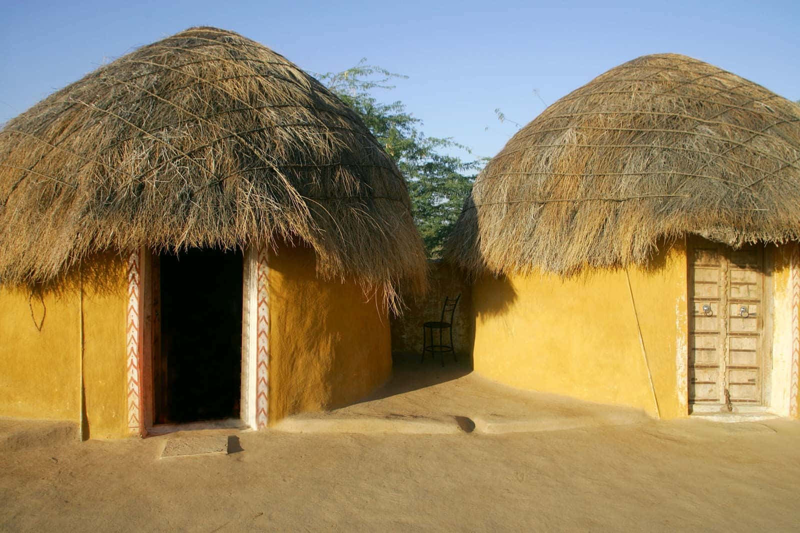 Rajasthan 桌布 壁紙 — 兩間圓頂形茅草屋頂和黃色泥牆的小屋，在乾燥的風景中矗立在晴朗的藍天下。