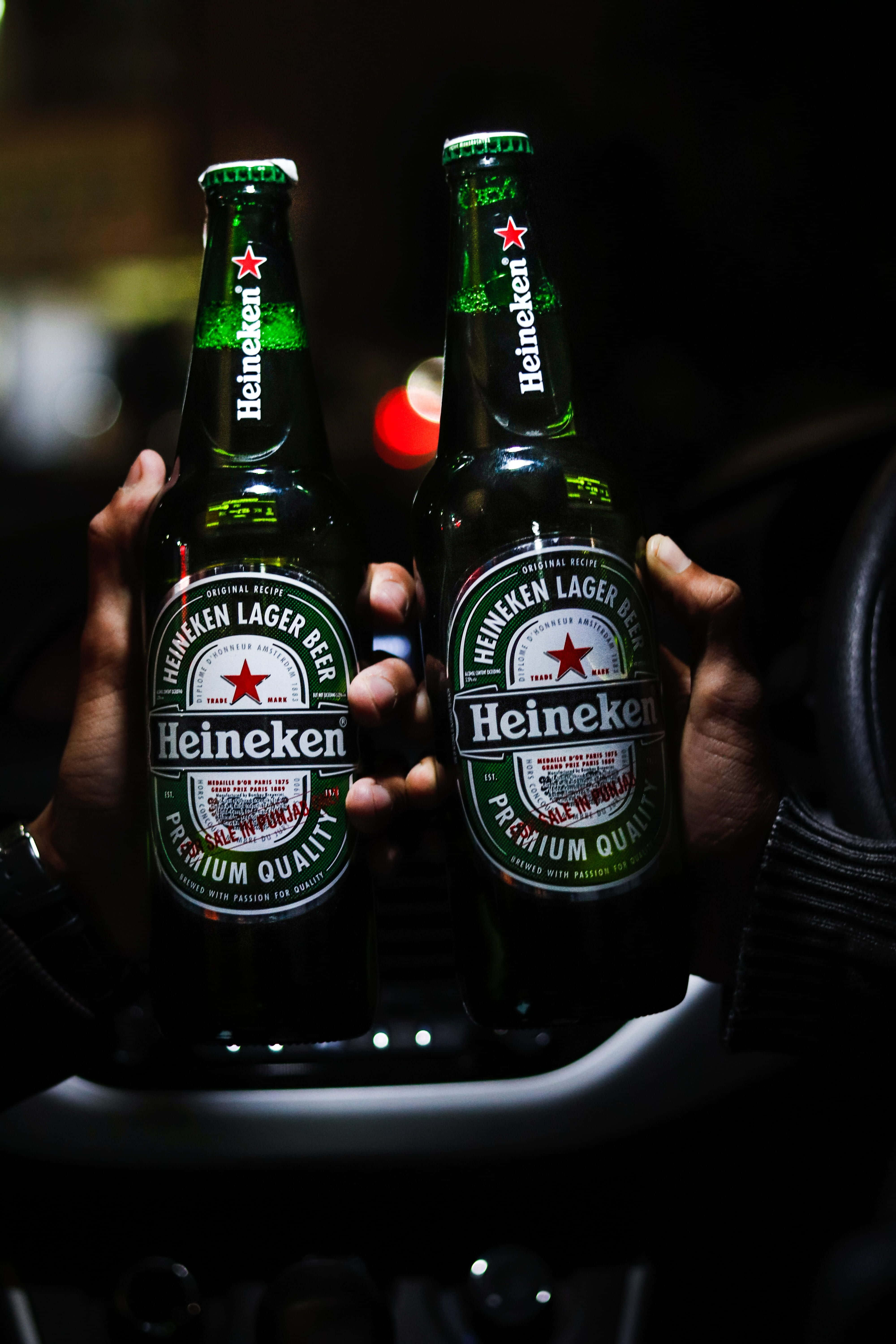Heineken 桌布 壁紙 — 兩隻手喺昏暗嘅車廂入面揸住綠色喜力啤酒樽，背景有模糊嘅燈光。