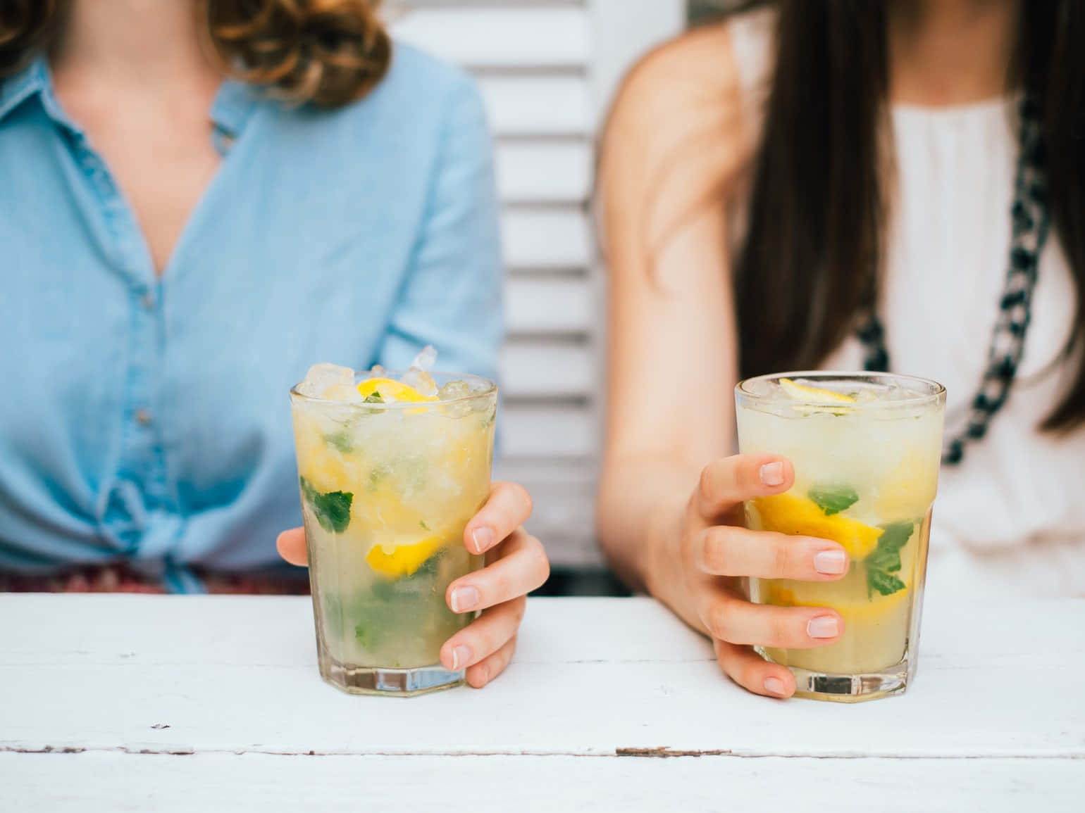 Beautiful Drink 桌布 壁紙 — 兩隻手喺白色木枱上拎住清新嘅檸檬薄荷飲品，背景有模糊嘅人影。
