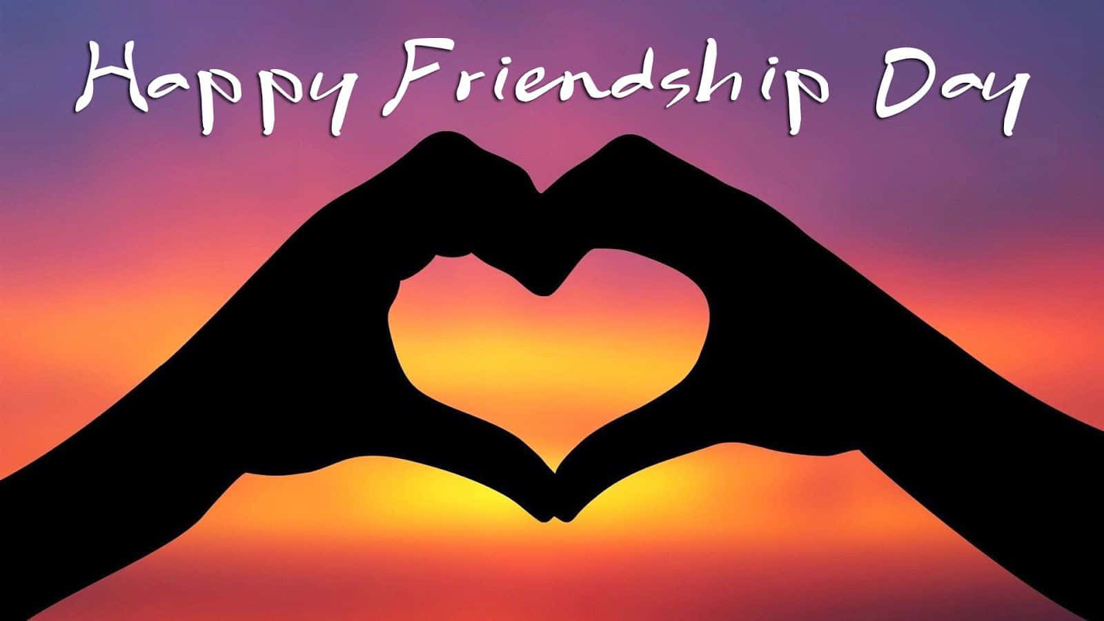 友誼日 桌布 壁紙 — 兩隻手在充滿活力的日落天空下形成心形，並帶有「Happy Friendship Day」文字。