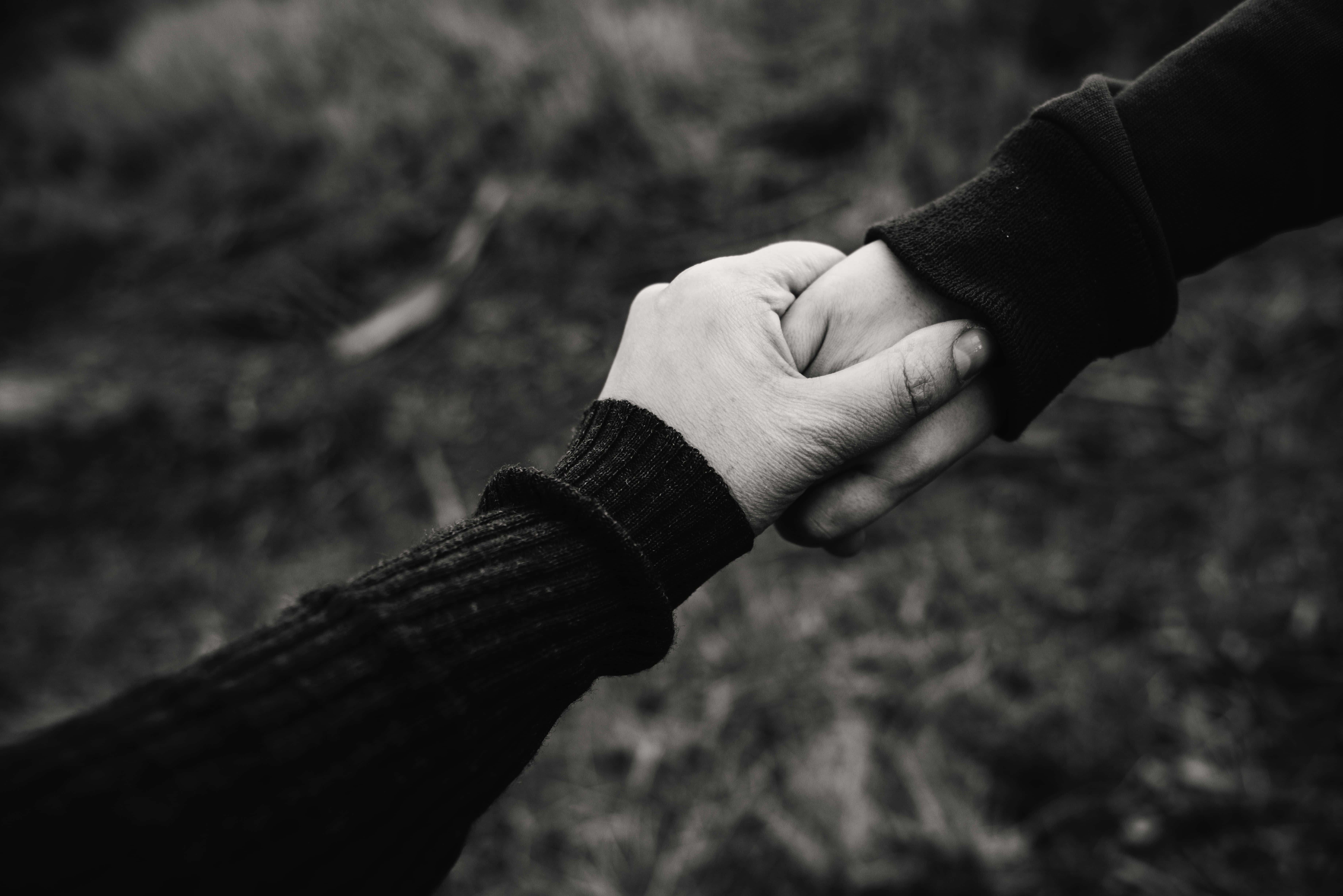 hands 桌布 壁紙 — 兩隻手在單色特寫中緊緊相握，在模糊的自然背景下傳達深刻的聯繫和支持。