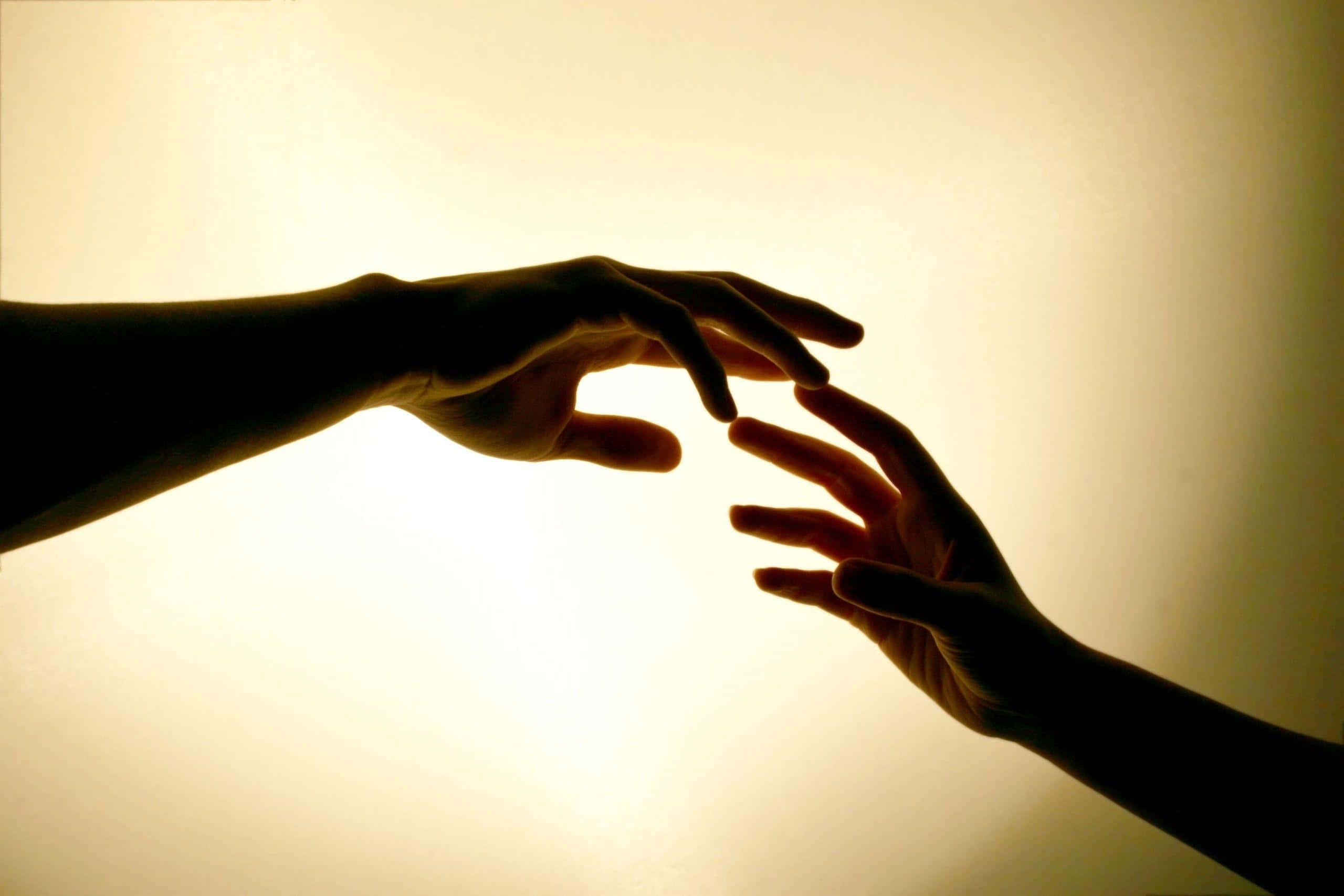hands 桌布 壁紙 — 兩隻手在溫暖發光的背景下互相伸向對方，處於溫柔的聯繫時刻。