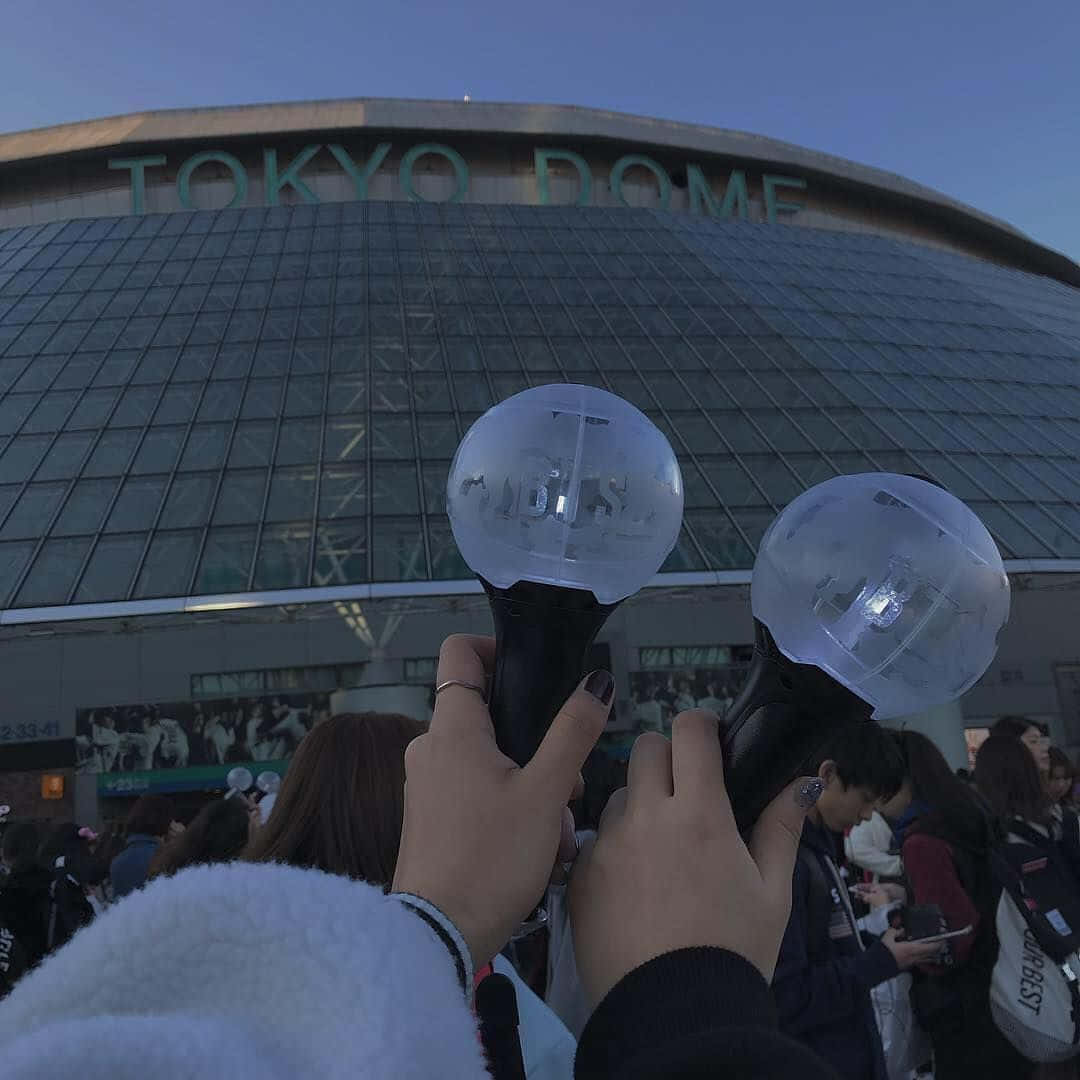 Bts Army Bomb 桌布 壁紙 — 兩隻手在黃昏時分於東京巨蛋前舉著發光的螢光棒，下方聚集了粉絲。