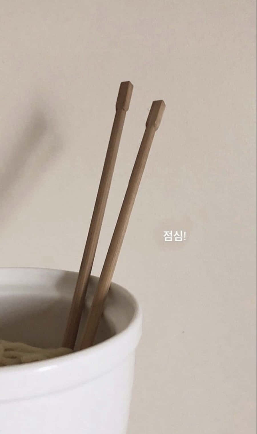 Korean Beige Aesthetic 桌布 壁紙 — 兩隻木筷子放在一個白色陶瓷碗裡，背景是素淨的米色牆壁，帶有柔和自然光線。