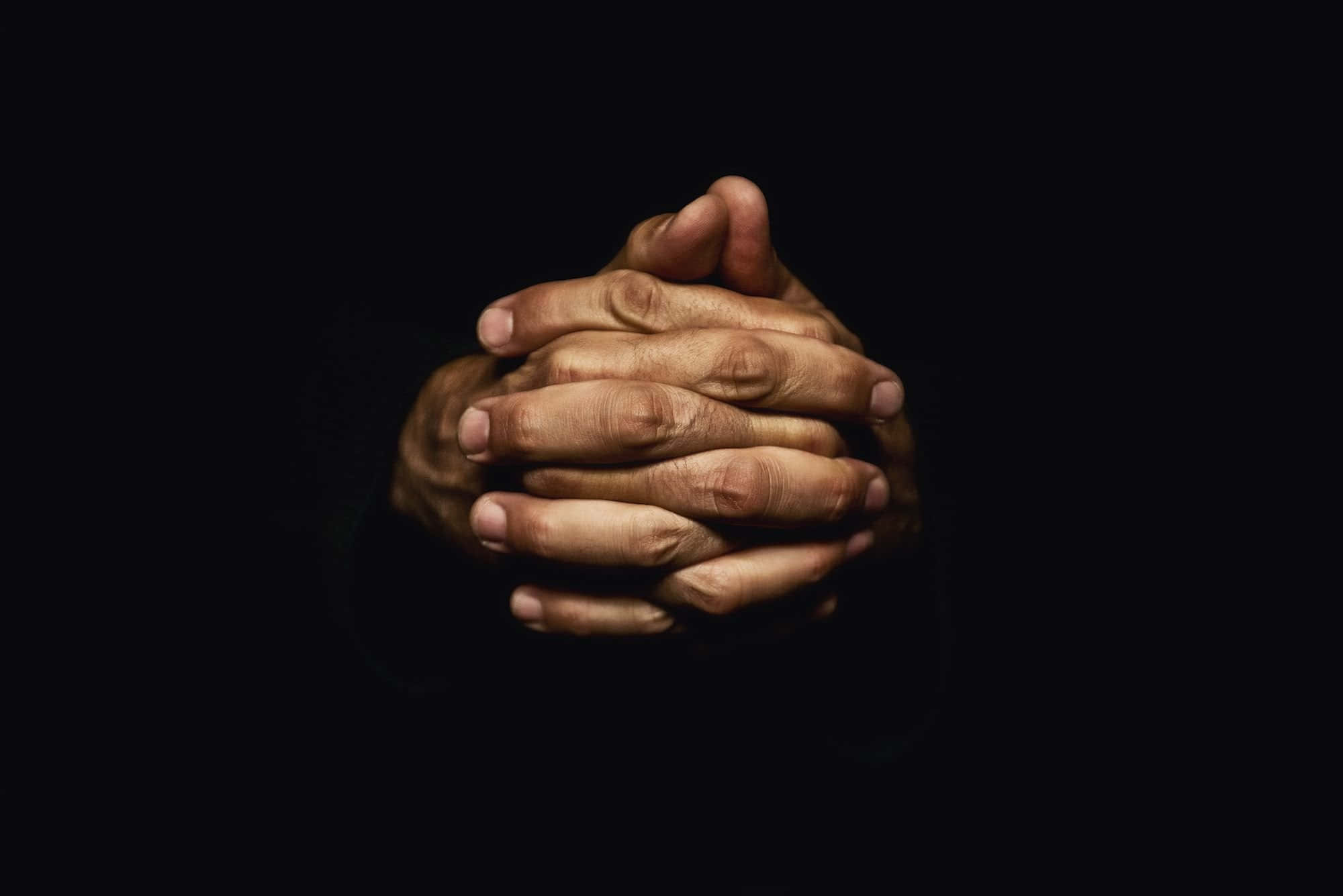 Dark Hand 桌布 壁紙 — 兩隻歷經風霜的手緊緊相握，以純黑背景襯托，柔和的方向性光線照亮。