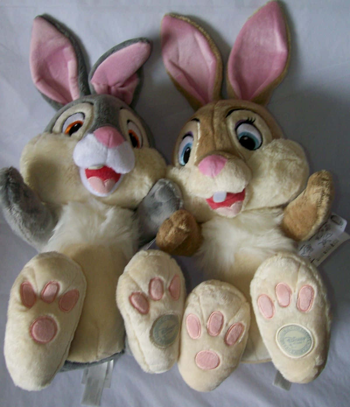 Miss Rabbit 桌布 壁紙 — 兩隻毛絨迪士尼兔子玩偶，粉紅色耳朵，微笑的臉，並排坐在白色表面上。