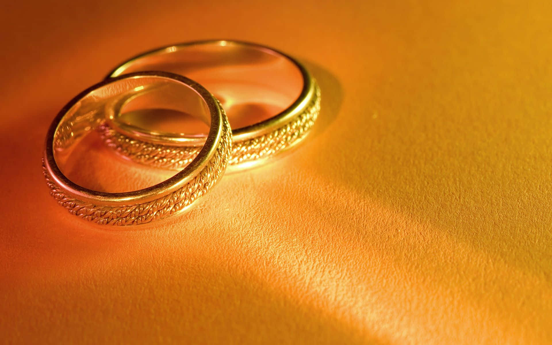 Ring 桌布 壁紙 — 兩隻華麗的金色結婚戒指放在溫暖的紋理表面上，沐浴在金色光線中。