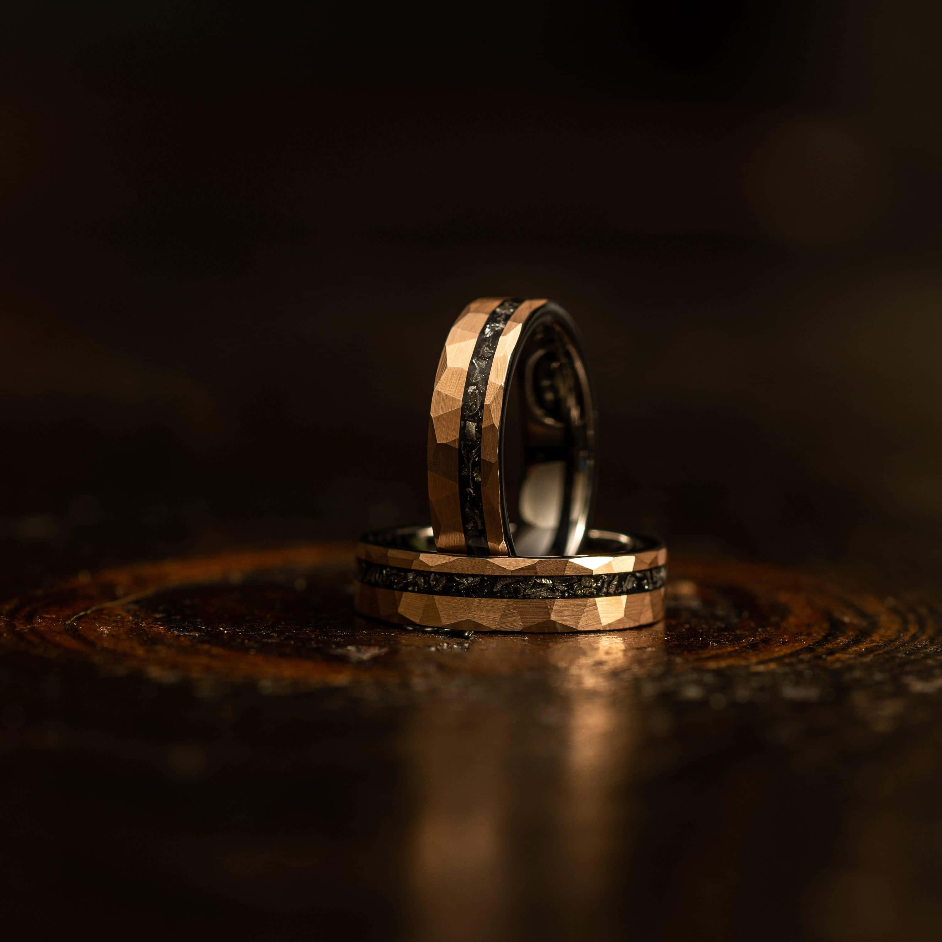 Ring 桌布 壁紙 — 兩隻金色和黑色紋理的結婚戒指優雅地放置在深色木質表面上，周圍有溫暖的環境光線。