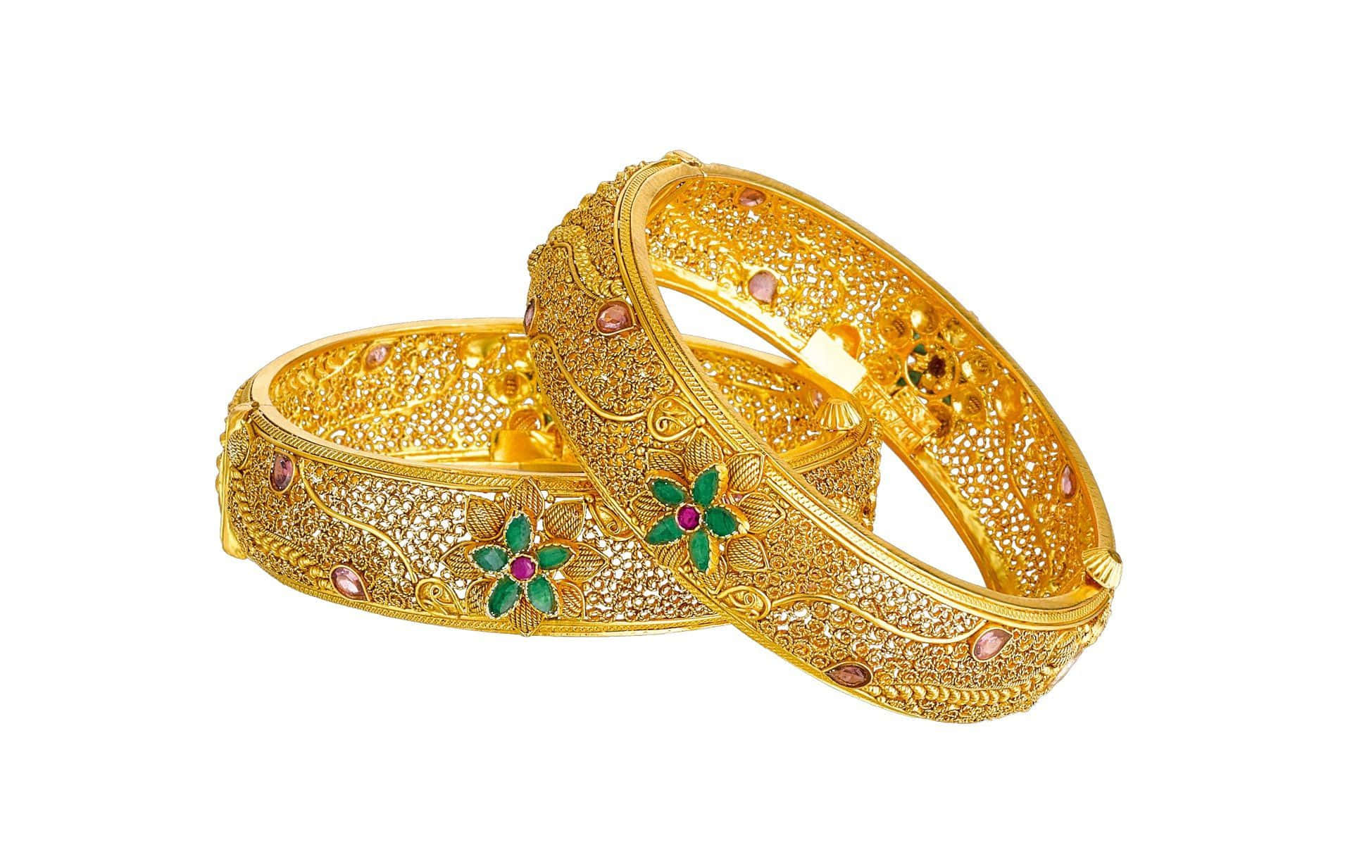 Jewelry Design 桌布 壁紙 — 兩隻飾有精細金銀絲花紋並鑲嵌綠色、粉紅色和紅色寶石的金手鐲，置於白色背景上。