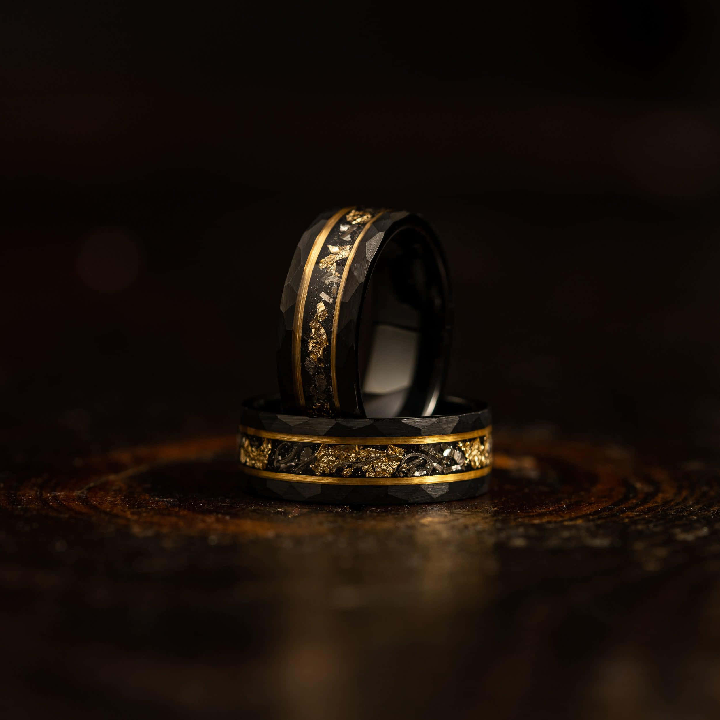 Ring 桌布 壁紙 — 兩隻黑色和金色的結婚戒指，帶有精緻的葉子圖案，優雅地放在深色木質表面上。