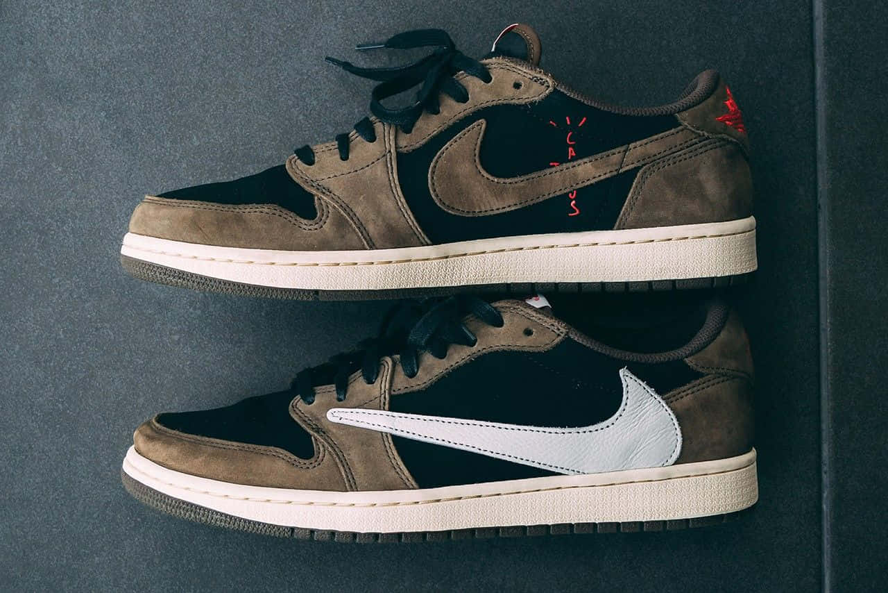 Travis Scott Jordan 1 桌布 壁紙 — 兩雙Travis Scott x Nike Air Jordan 1運動鞋，採用棕色、黑色和白色麂皮，帶有紅色塗鴉細節，掛在深灰色牆上。