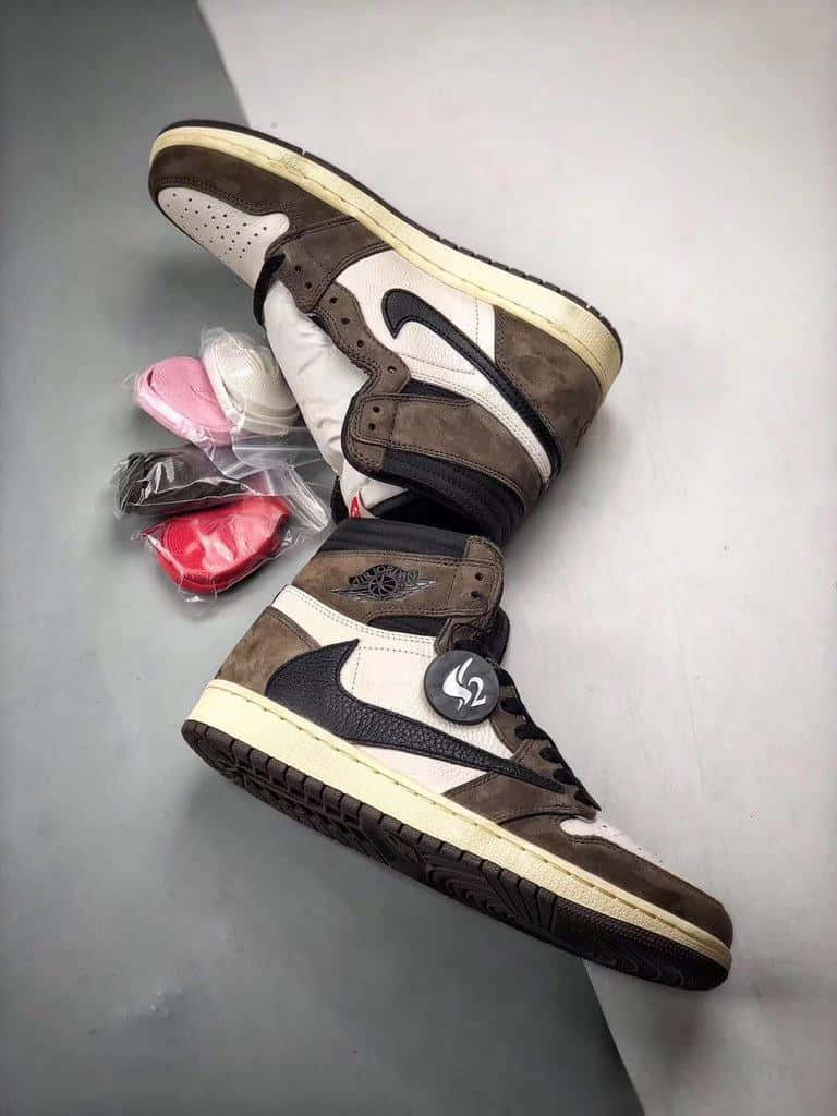 Travis Scott Jordan 1 桌布 壁紙 — 兩雙棕色和白色的高筒運動鞋，帶有黑色點綴和原裝包裝，放置在灰色表面上。
