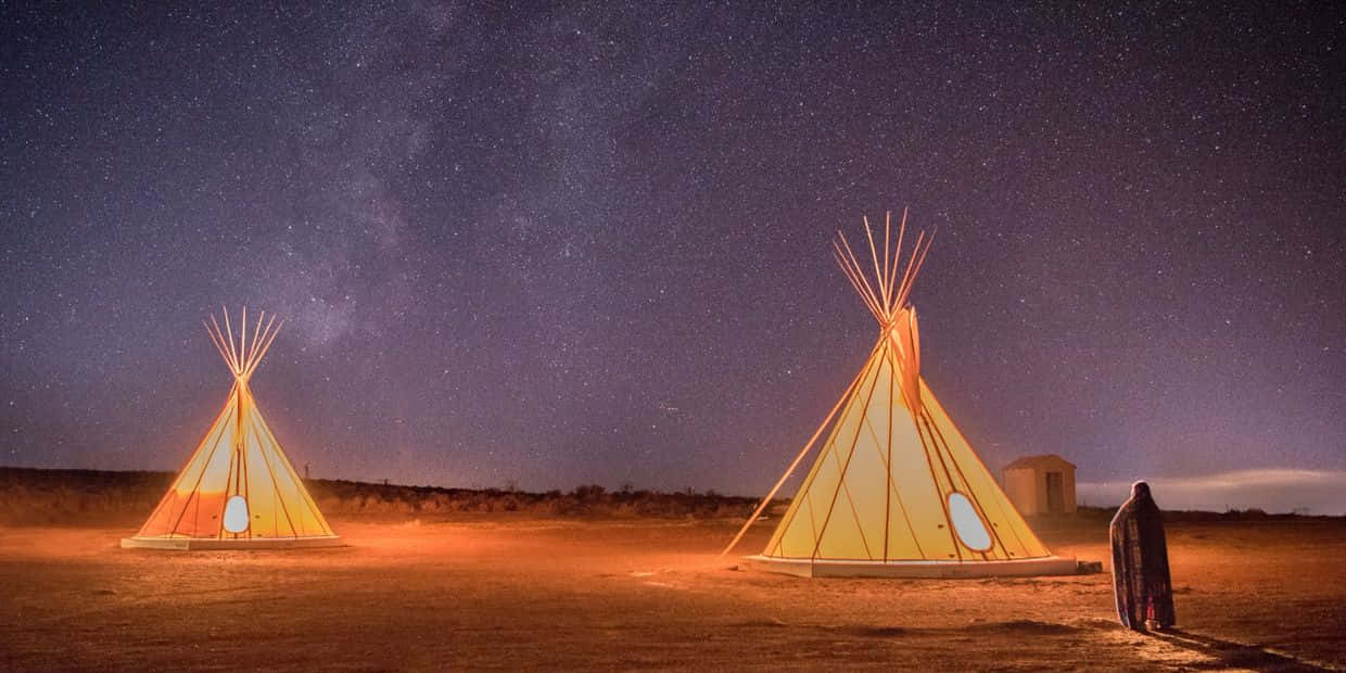 星空下兩個發光的帳篷，沙漠中有一個人站在附近。