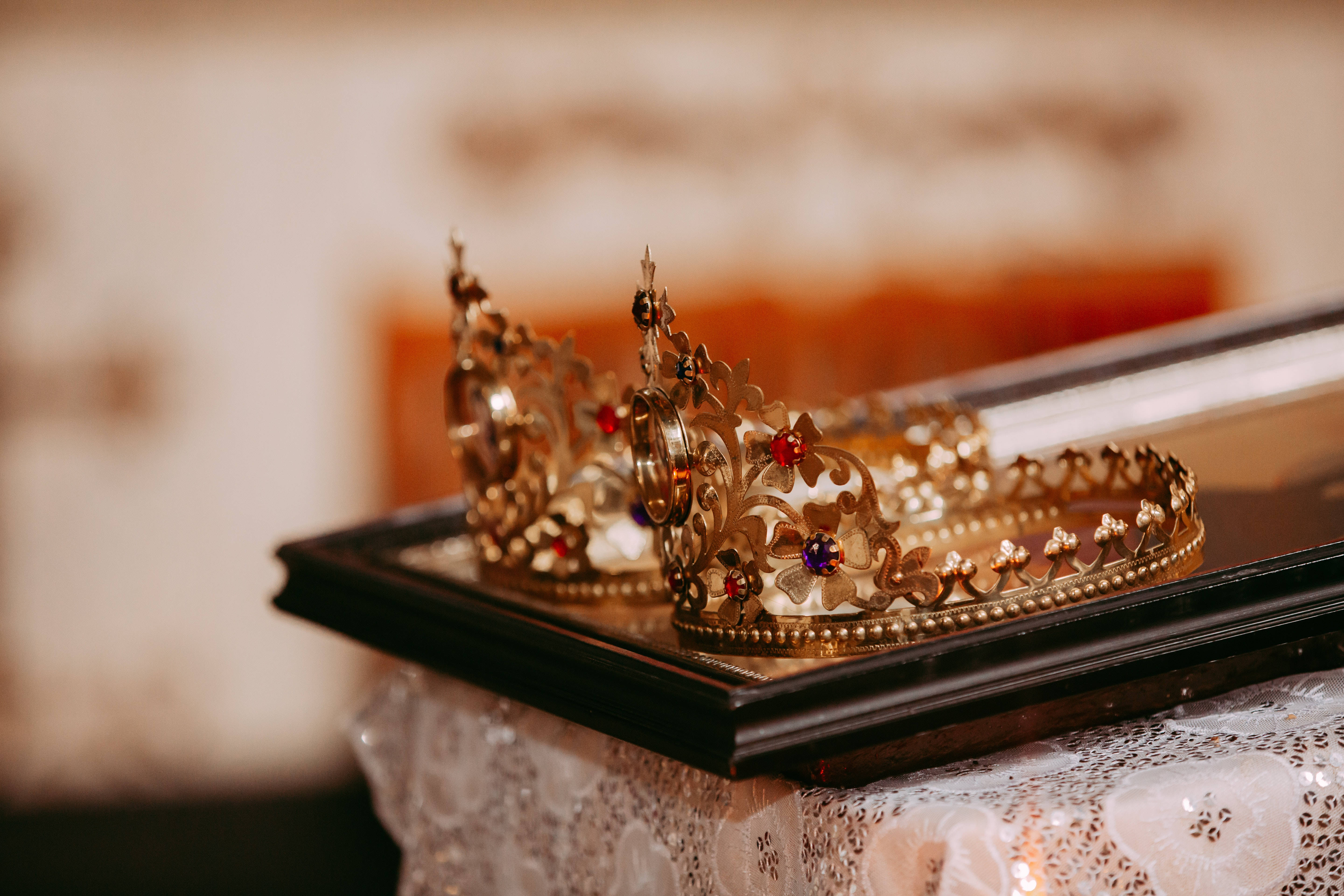 King And Queen 桌布 壁紙 — 兩頂華麗的金色皇冠，鑲有紅色和藍色寶石，優雅地放置在一個覆蓋著蕾絲的深色木盒上。
