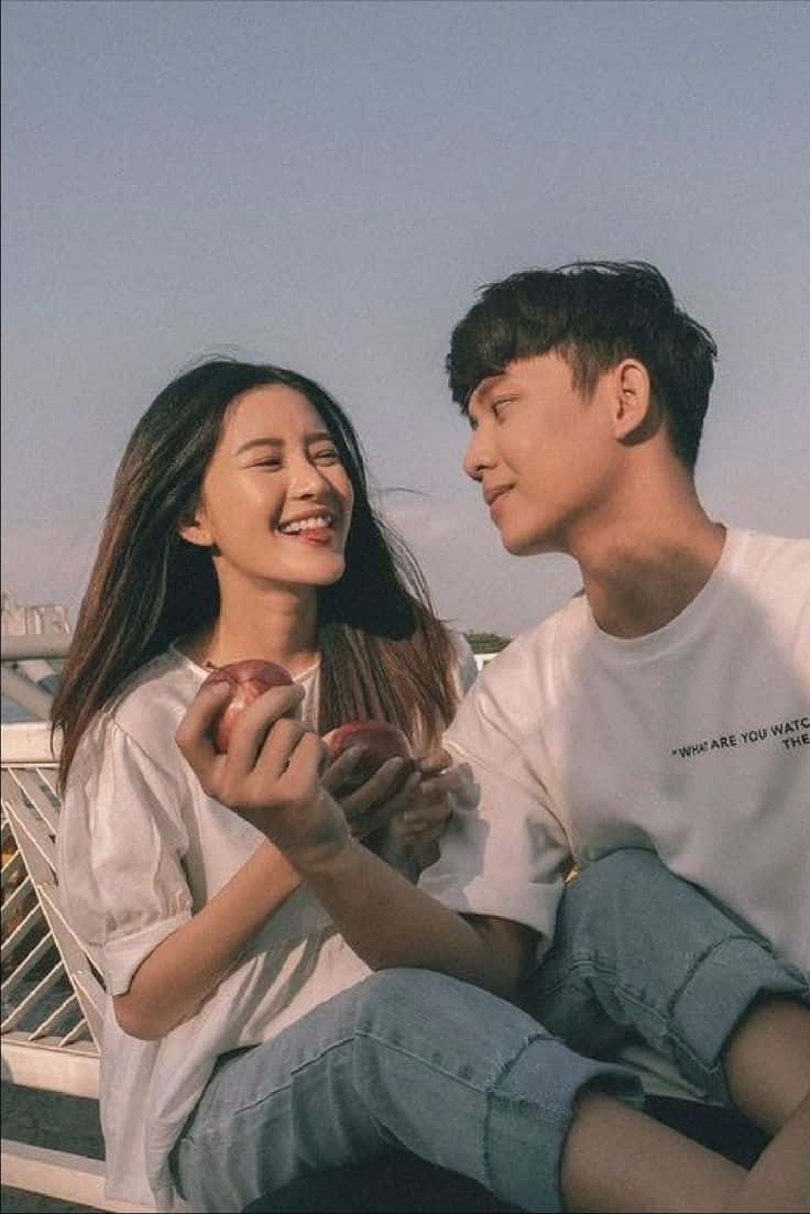 兩顆心，一份愛 壁紙 — 一對年輕情侶在黃金時刻於屋頂上拿著蘋果，溫暖地微笑著。