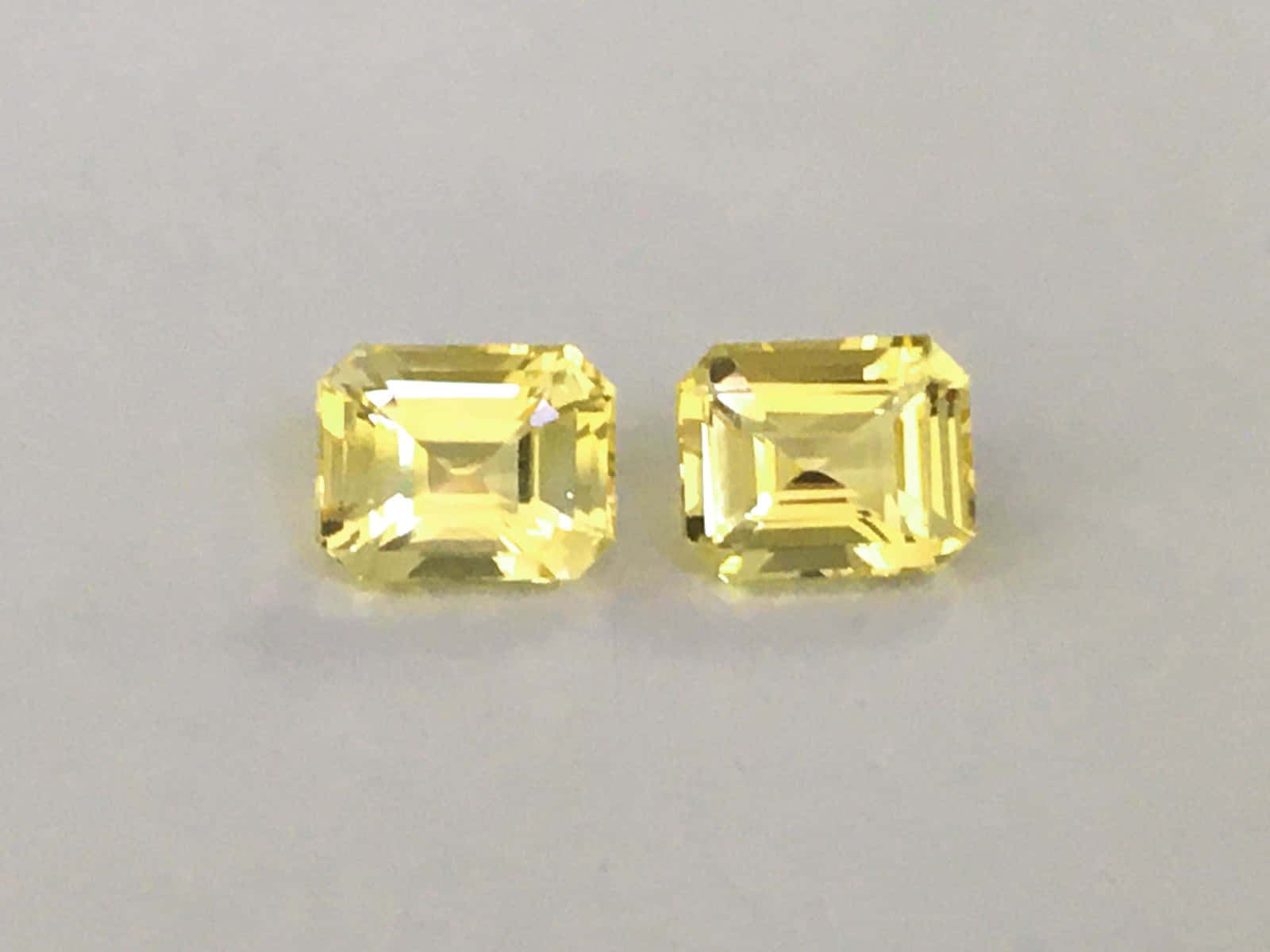 Yellow Sapphire 桌布 壁紙 — 兩顆璀璨的黃色祖母綠切割寶石在柔和的中性背景上閃耀著精確的刻面。