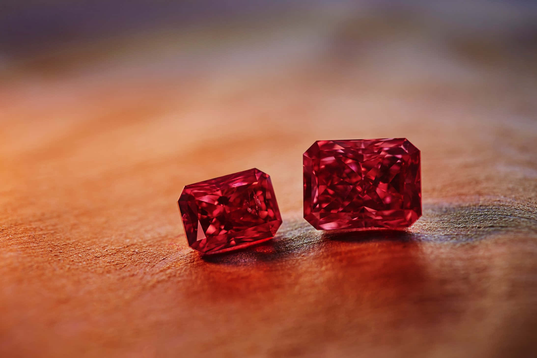 Red Diamond 桌布 壁紙 — 兩顆閃耀的紅色祖母綠在溫暖的木質表面上，於柔和的金色光芒下散發出火熱般的光彩。
