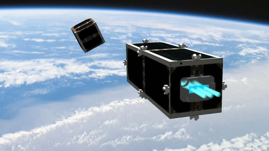 Space Debris 桌布 壁紙 — 兩顆黑色立方體衛星在地球藍白雲層覆蓋的表面上方軌道漂浮，其中一顆發出明亮的藍色光束。