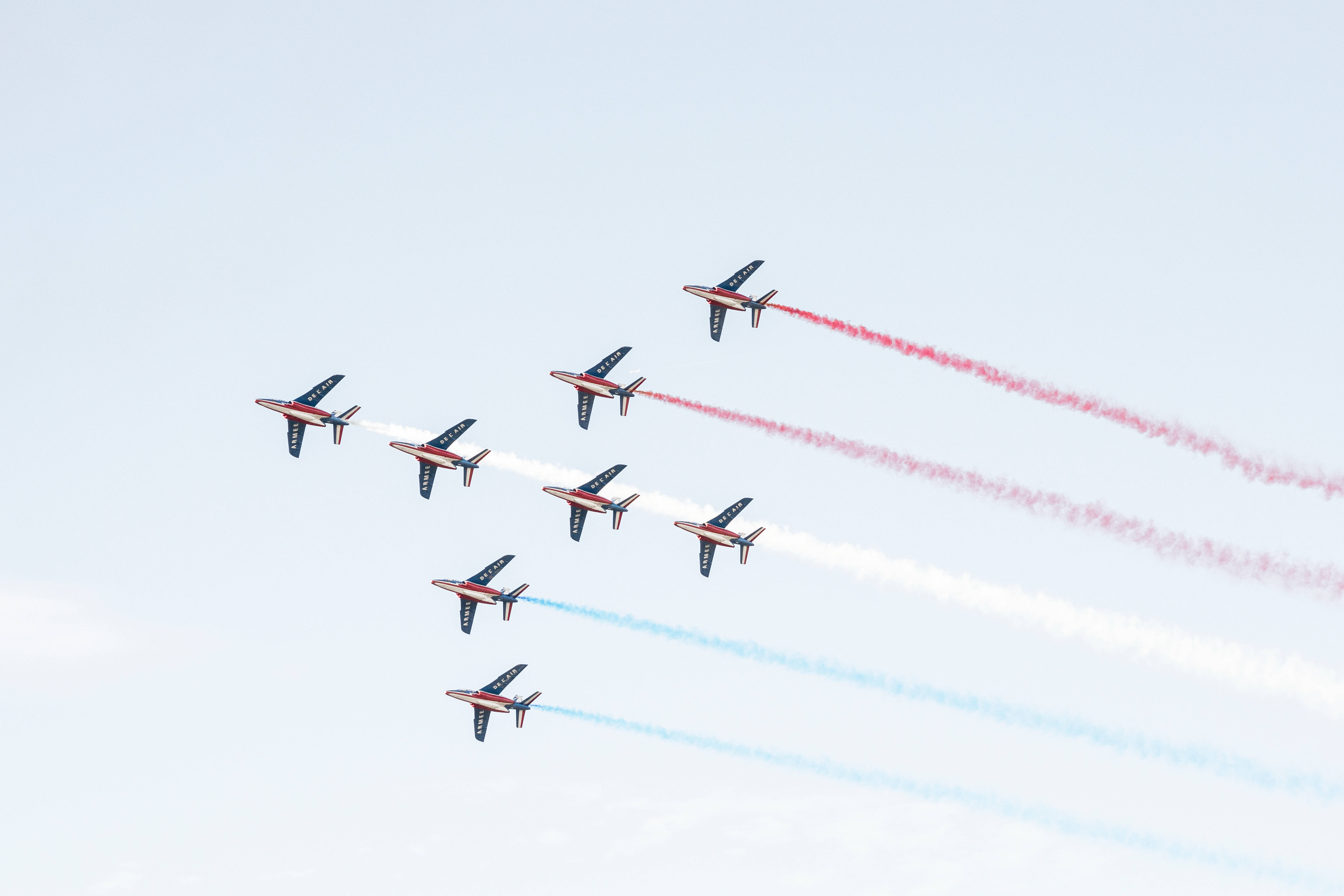 八架小型飛機特技飛行 壁紙 — 七架戰鬥機以緊密編隊飛過蒼白的天空，留下紅色、白色和藍色的煙霧痕跡。
