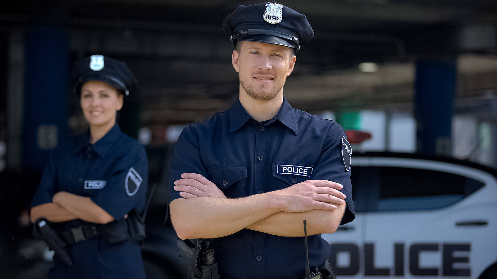 兩名警察微笑交叉雙臂站在警車前。
